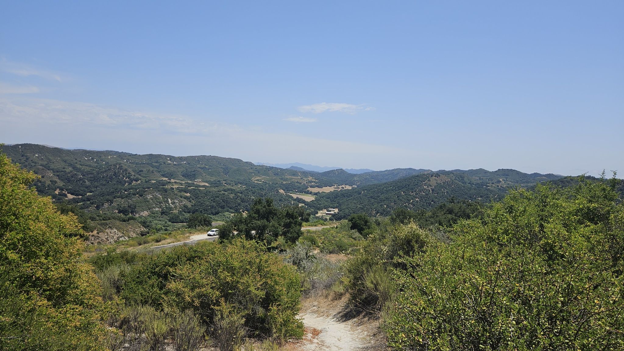 Dirt path leading through green hills with a distant white car. - High Ridge Loop
