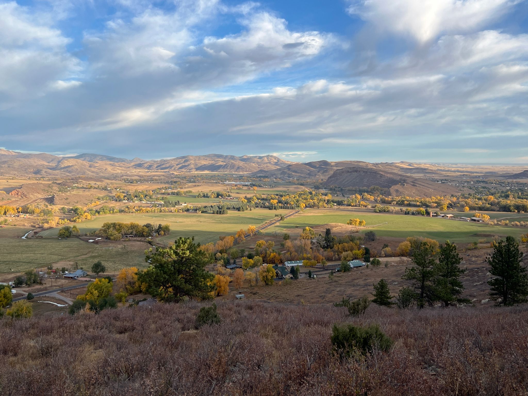 Panoramic view of a valley with fields, trees, and distant mountains under clouds. - Reservoir Ridge North Loop Trail