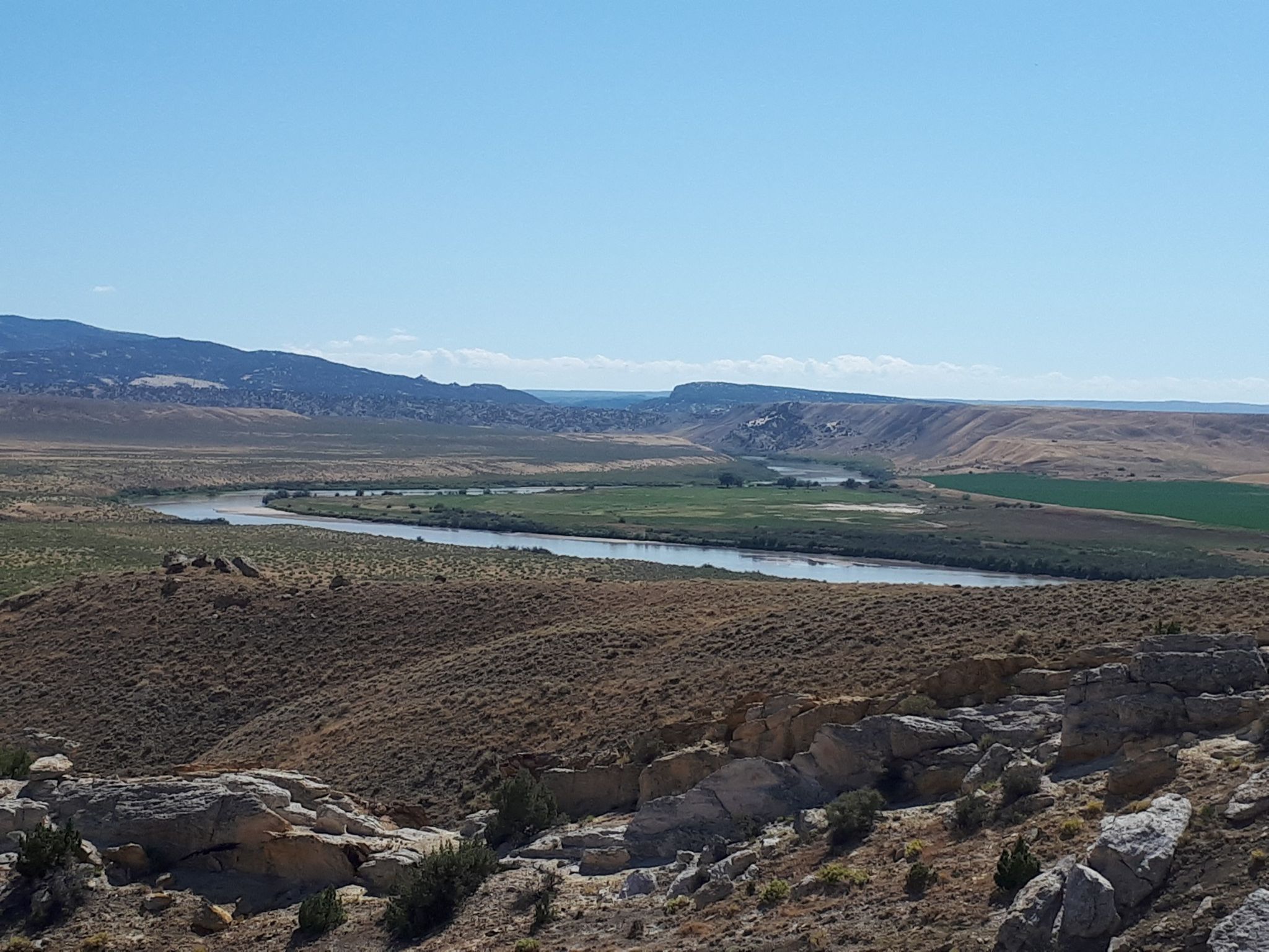 A wide river winds through a green valley surrounded by arid hills. - Fossil Discovery Trail – Dinosaur National Monument