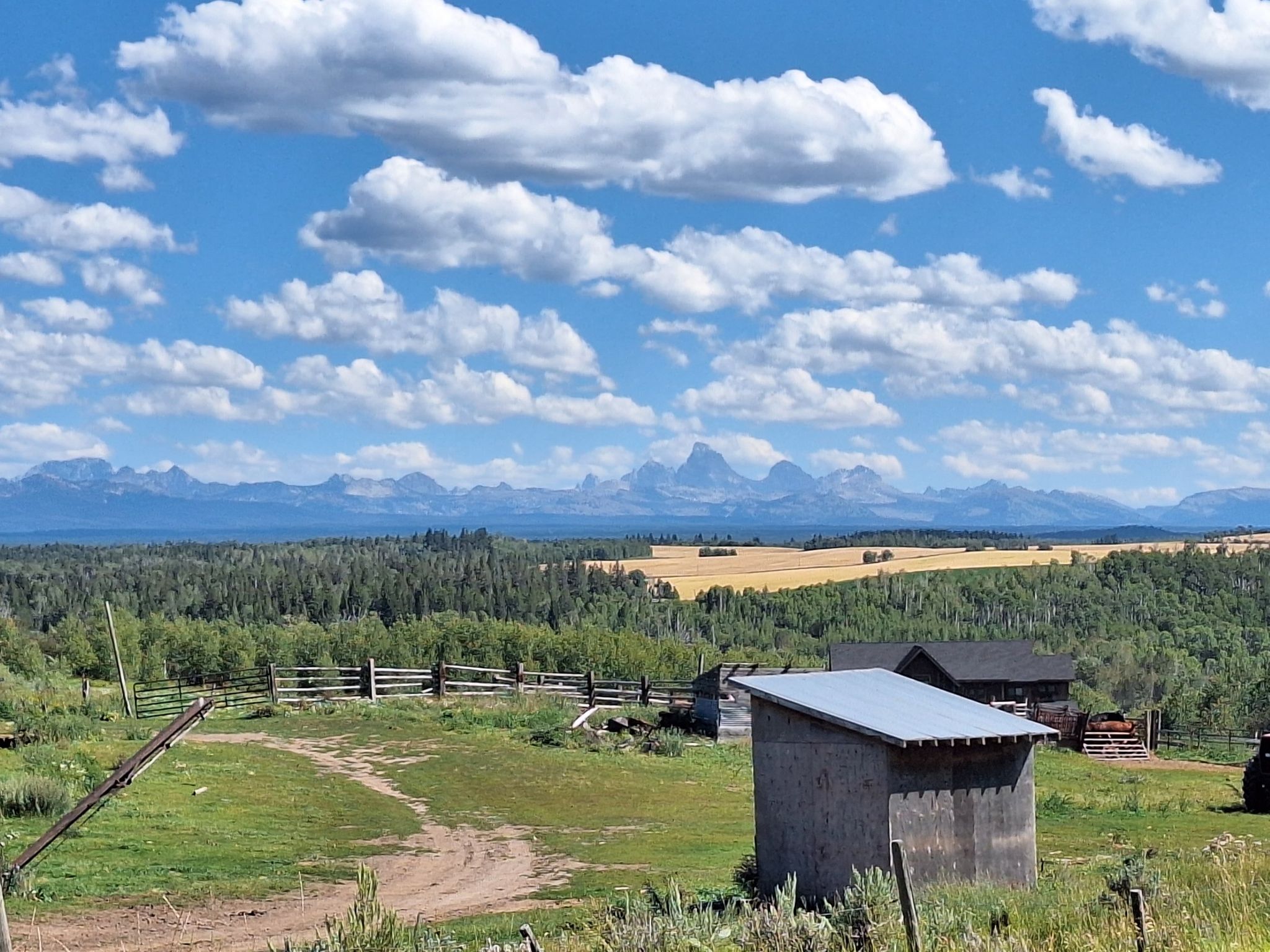 Rural scene with fields, buildings, and majestic mountains under a cloudy sky. - Great Divide Mountain Bike Route