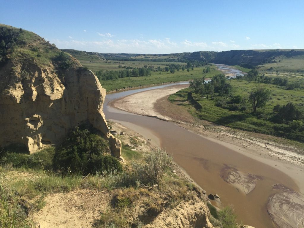 A winding river flows past an eroded rock formation in a green valley. - Wind Canyon Trail