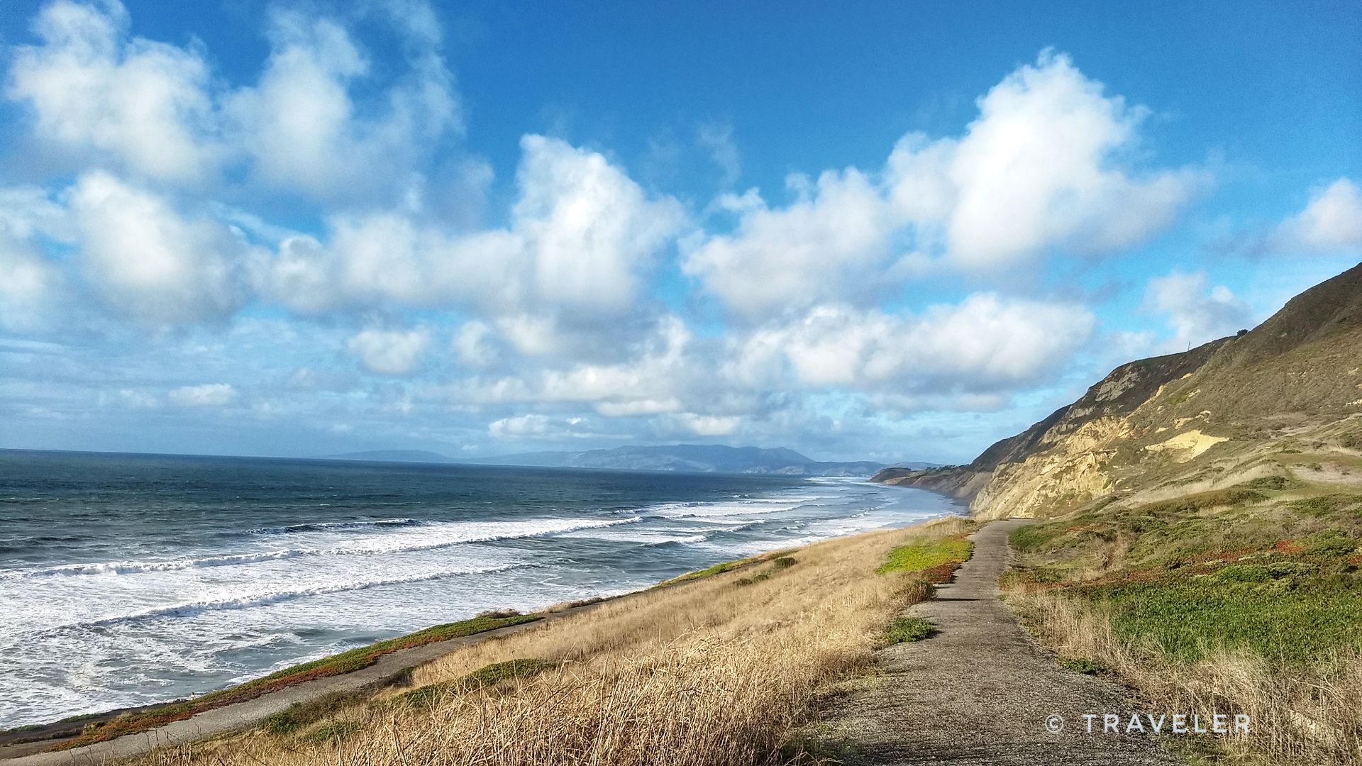 Sunny coastal view with crashing waves, a dirt path, and a grassy hillside. - Mussel Rock Trail
