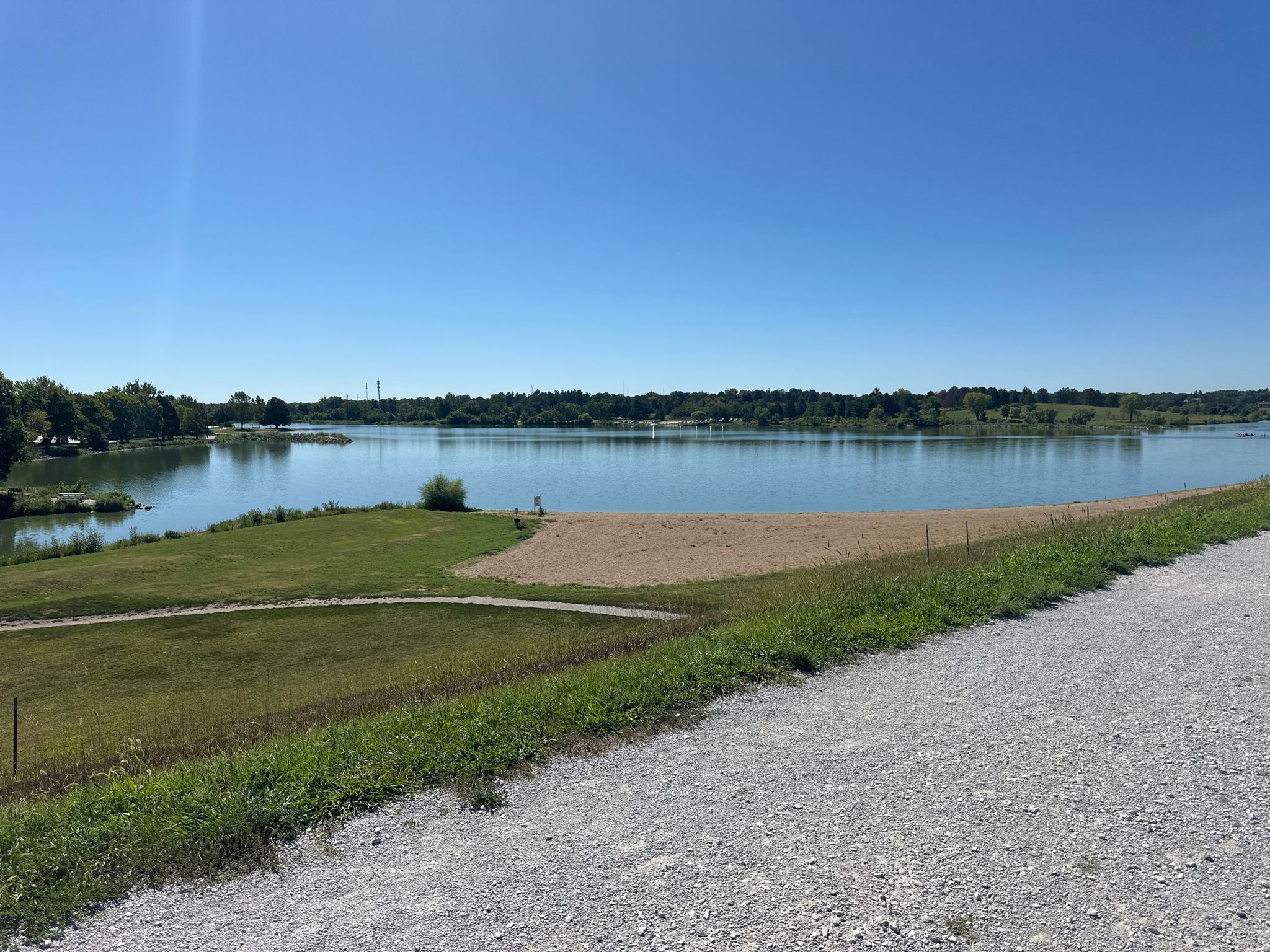 Sunny day over a wide lake with a sandy beach and green grass. - Holmes Lake Park loop