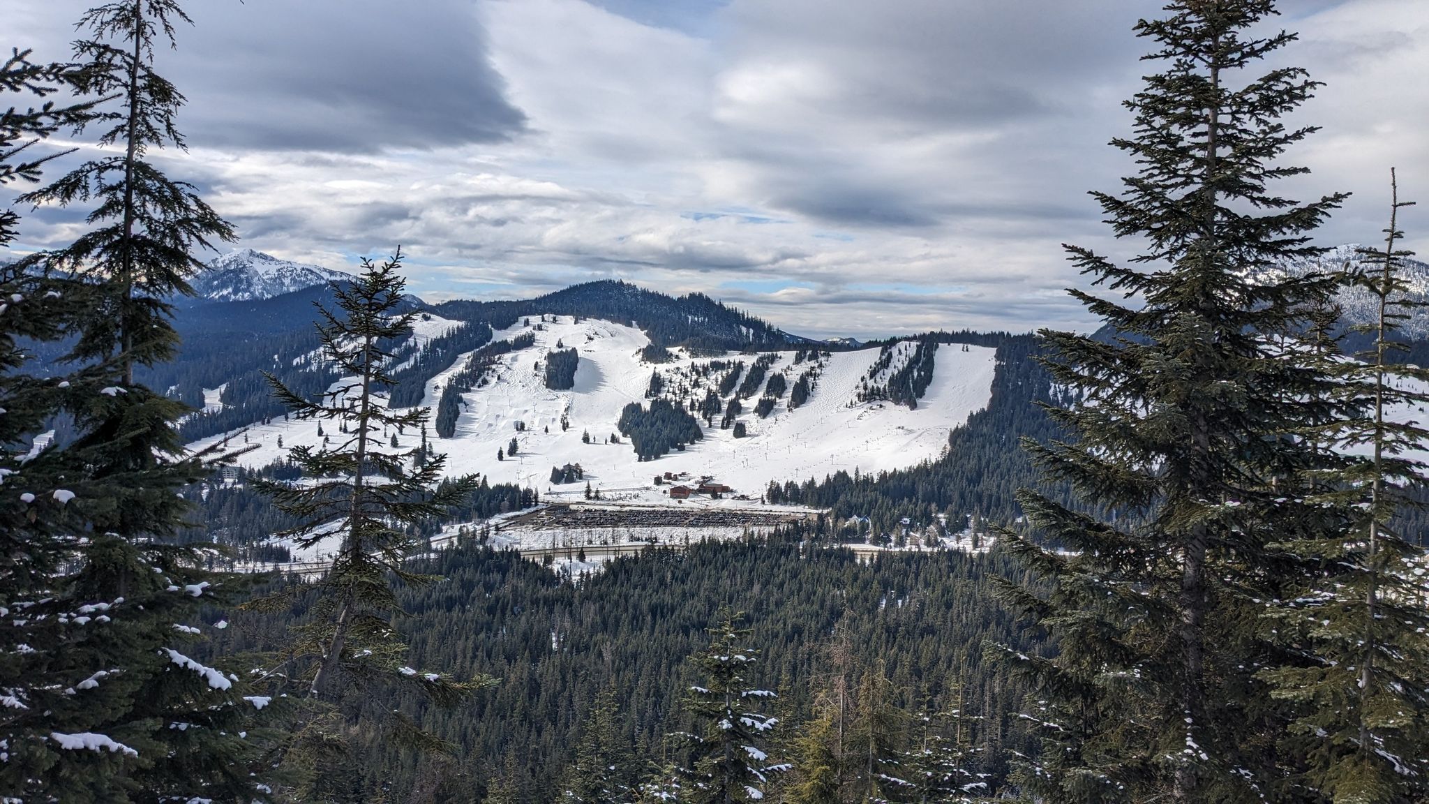 Overcast view of snow-covered mountains with evergreen forests and cleared slopes. - Kendall Peak Lakes Trail