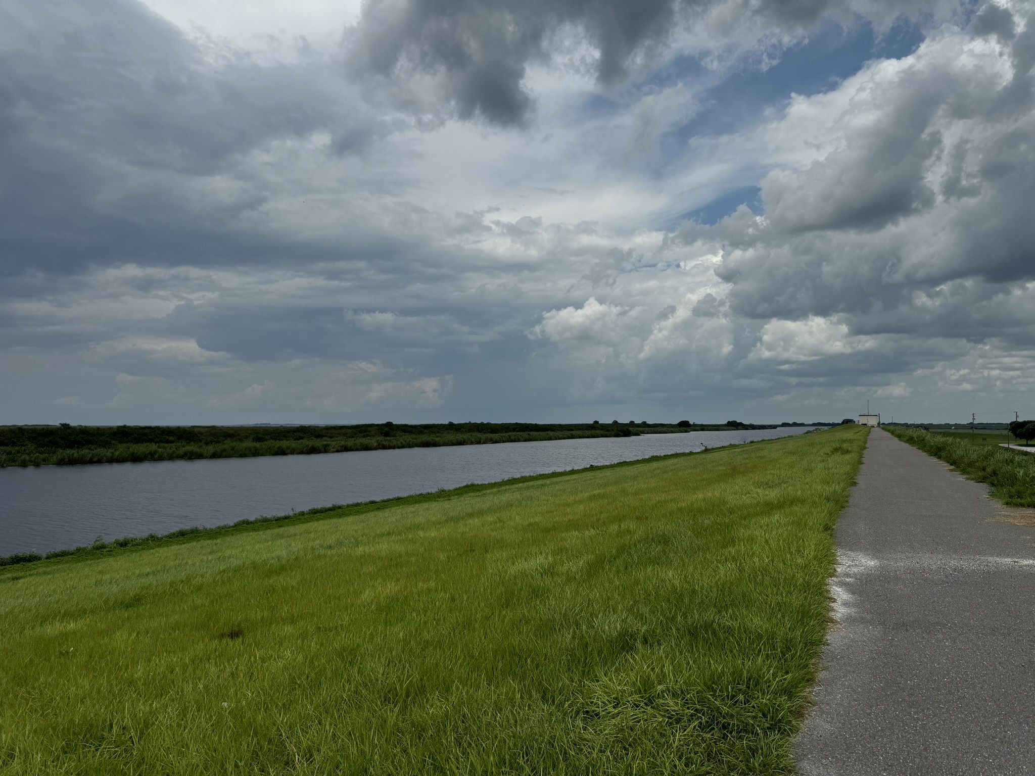 Paved path alongside a wide canal under a cloudy, overcast sky. - Lake Okeechobee Scenic Trail