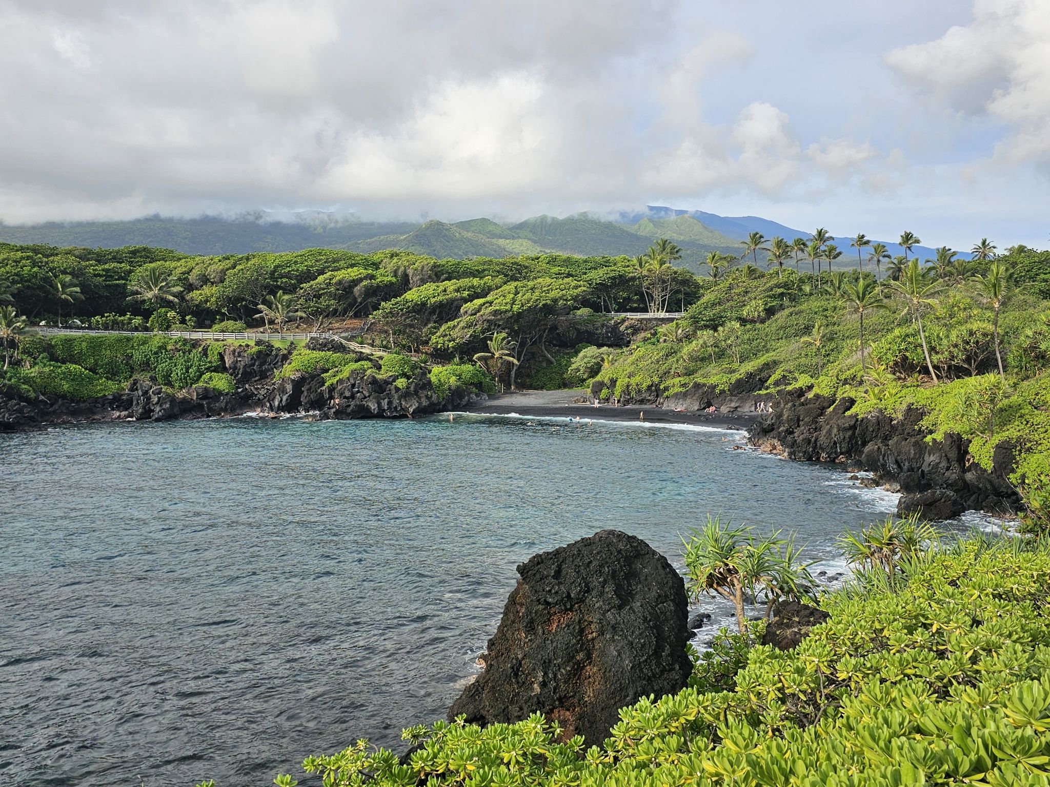 Bay with black sand beach, lush green hills, and cloudy sky. - Black Sand Beach – Piilani Trail loop from Waiʻānapanapa State Park