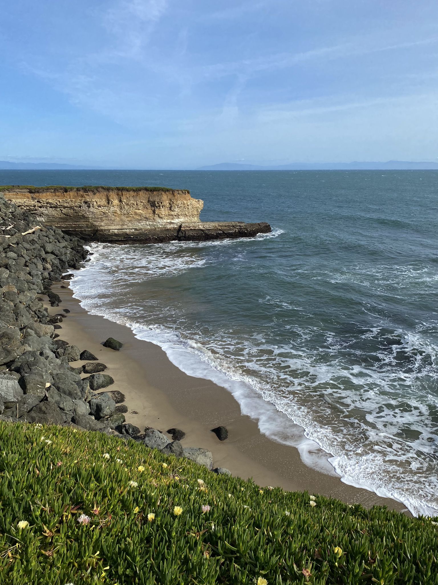 Sunny coastal view with waves breaking on a sandy beach and rocky cliffs. - West Cliff Drive Loop