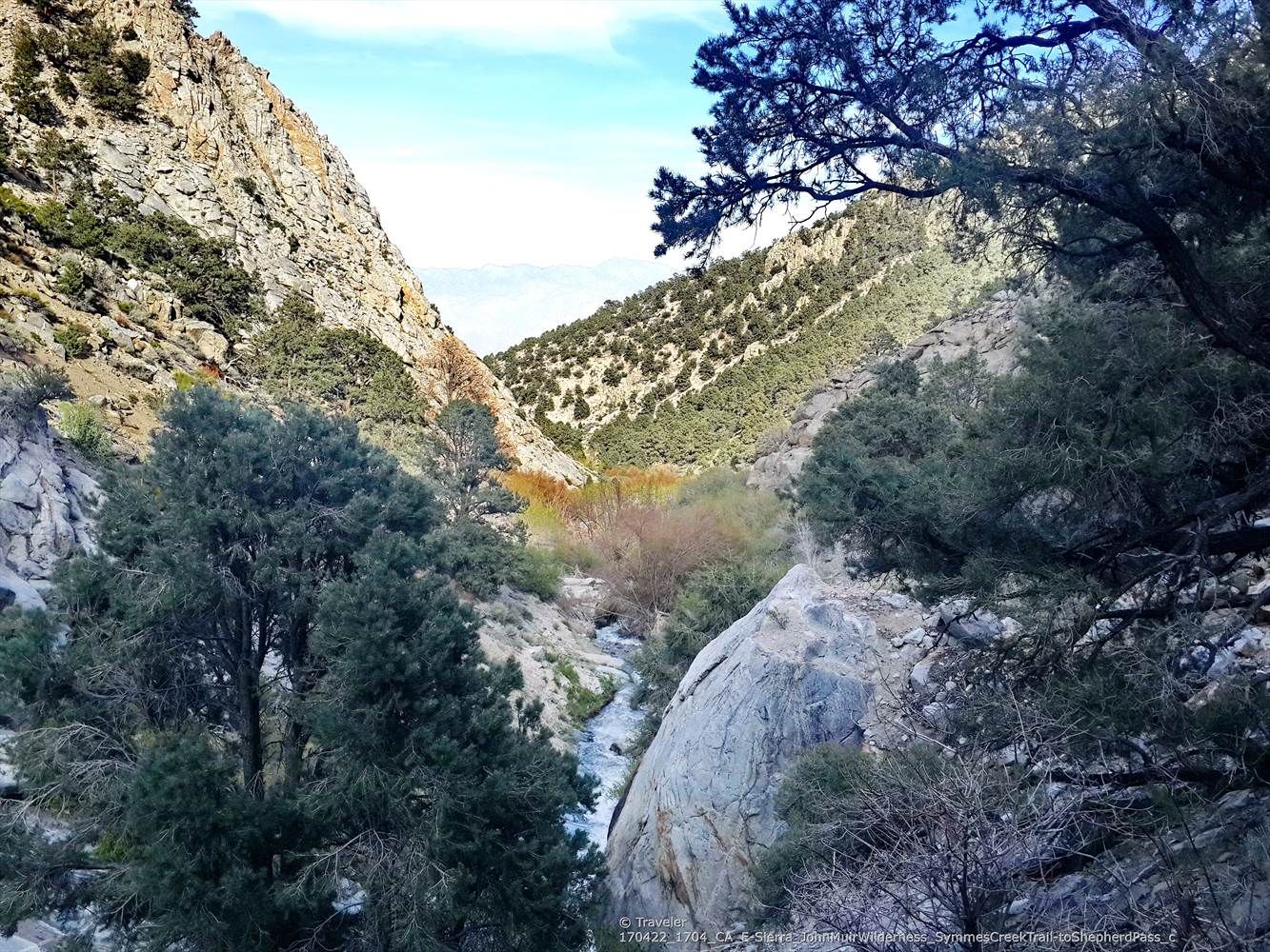A narrow mountain valley with steep rocky slopes, green trees, and a flowing stream. - Shepherd Pass Trail
