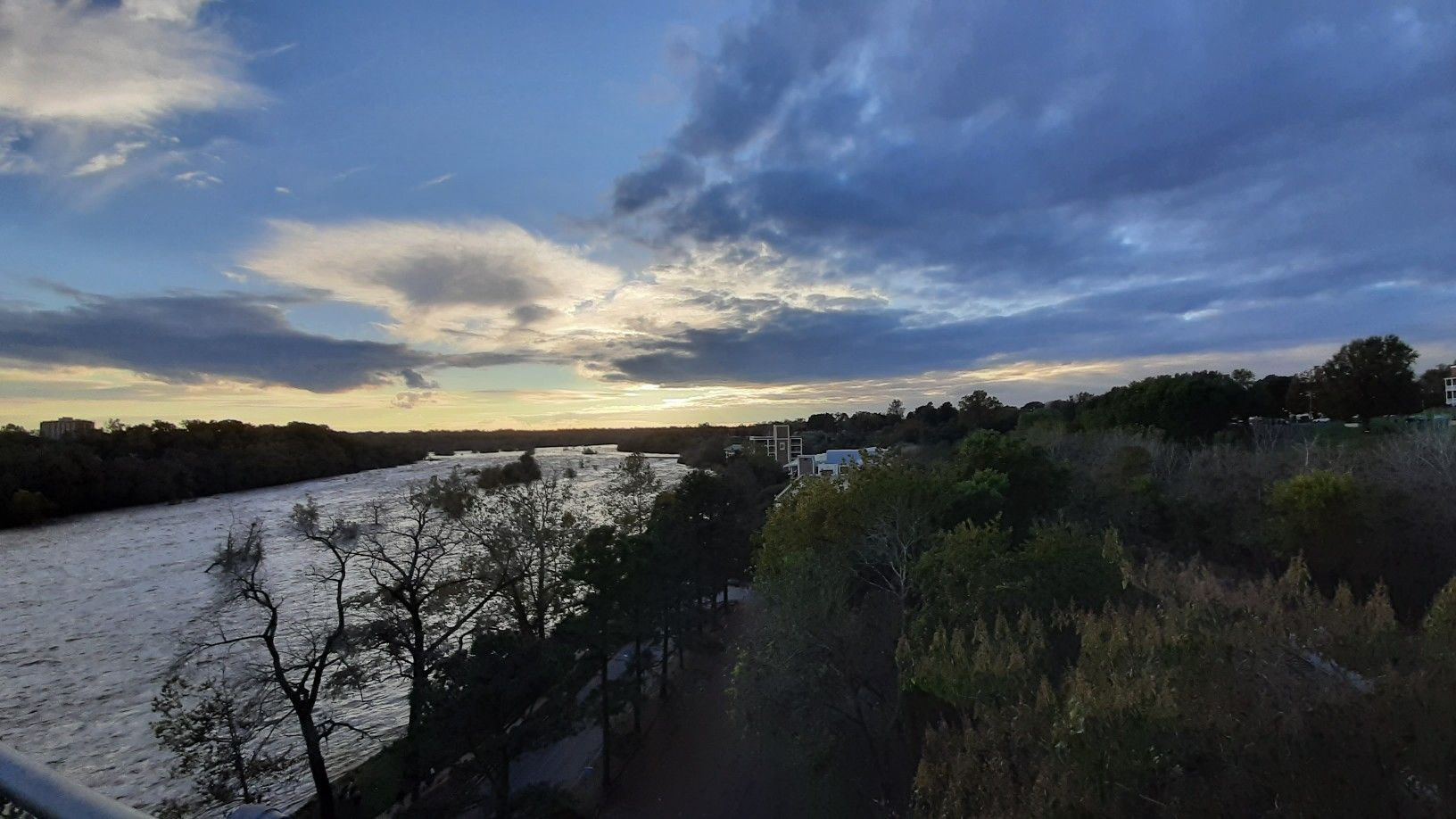 Wide river flows through a forested landscape under a dramatic cloudy sunset. - Lewis G. Larus Park – Robert Lee Bridge loop from Richmond Main Street