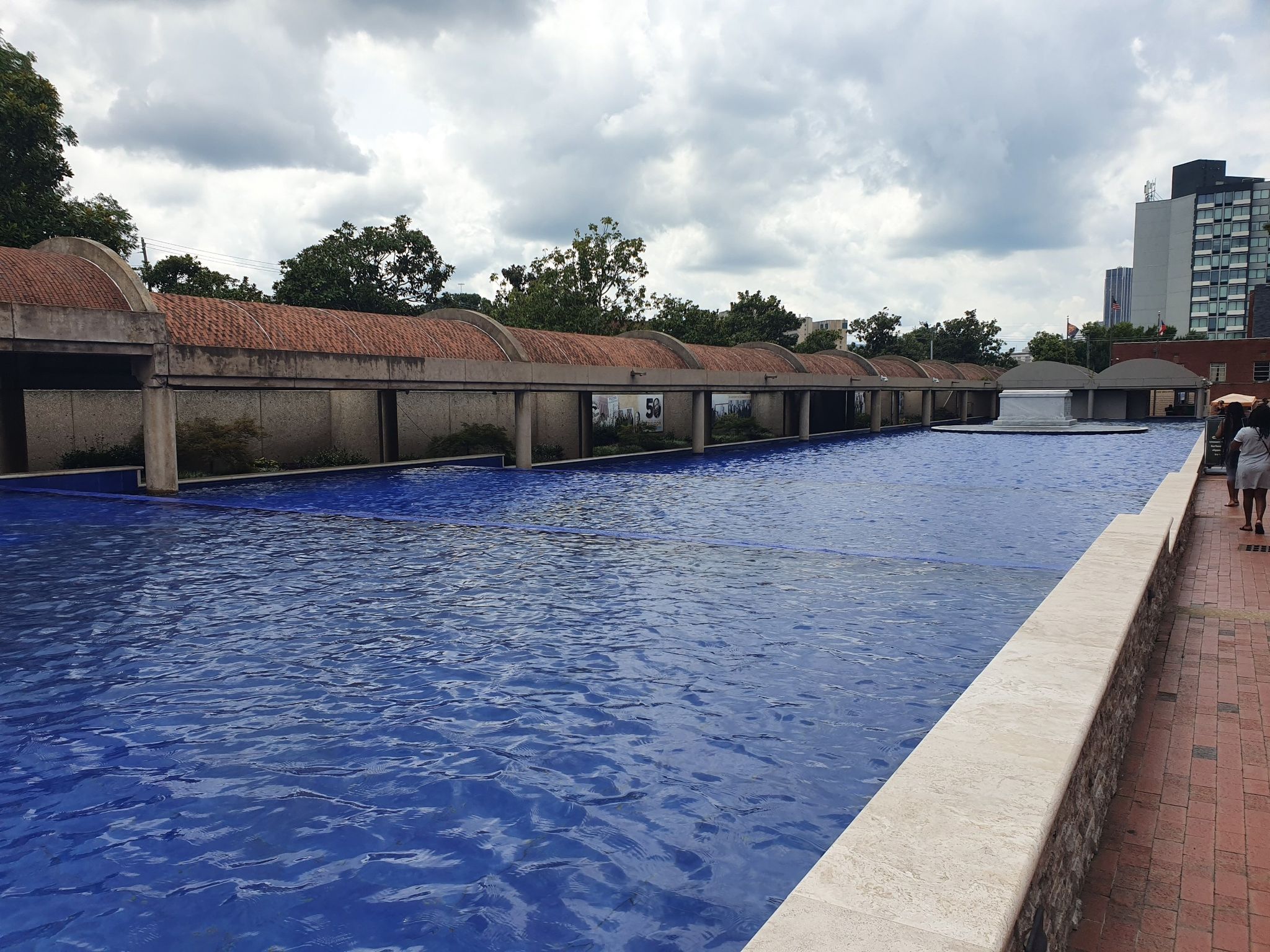A long blue reflecting pool with arched structures under a cloudy sky. - Sweet Auburn District Walking Tour