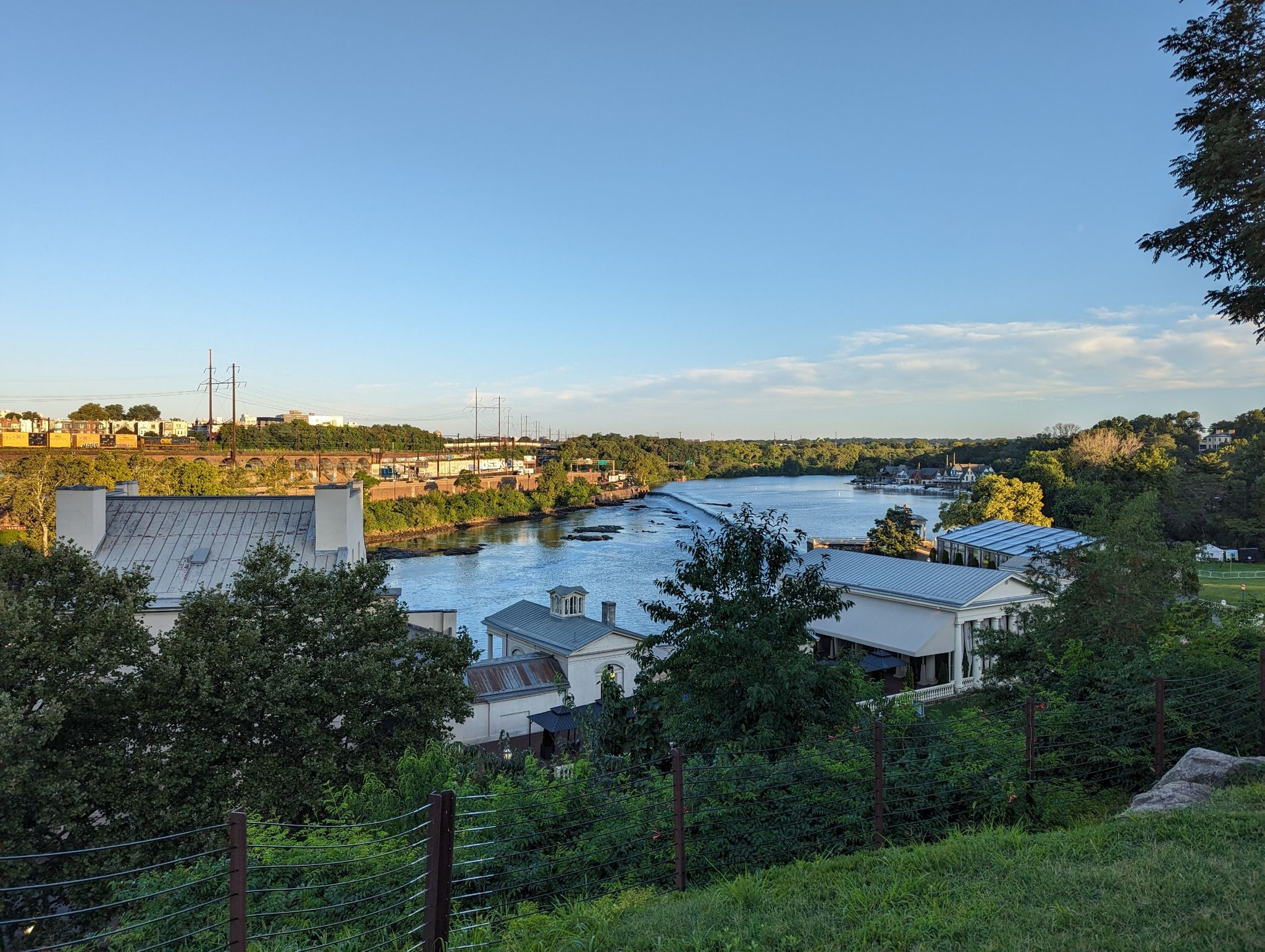 Scenic view of a wide river flowing past houses and green hills at sunset. - LOVE Sculpture, Love Park – Huge murals loop from Spring Garden
