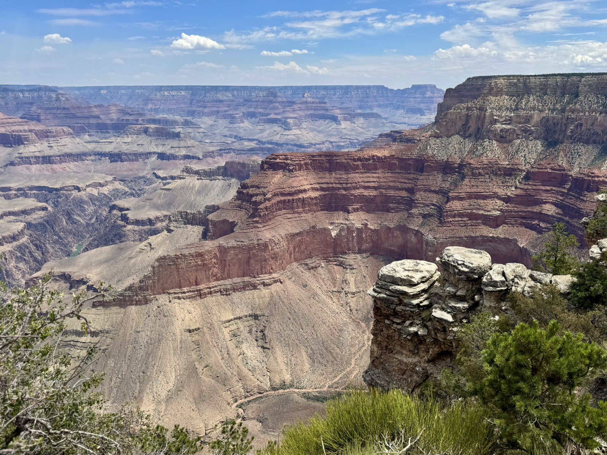 Vast layered canyon under bright blue sky with scattered clouds. - Rim Trail