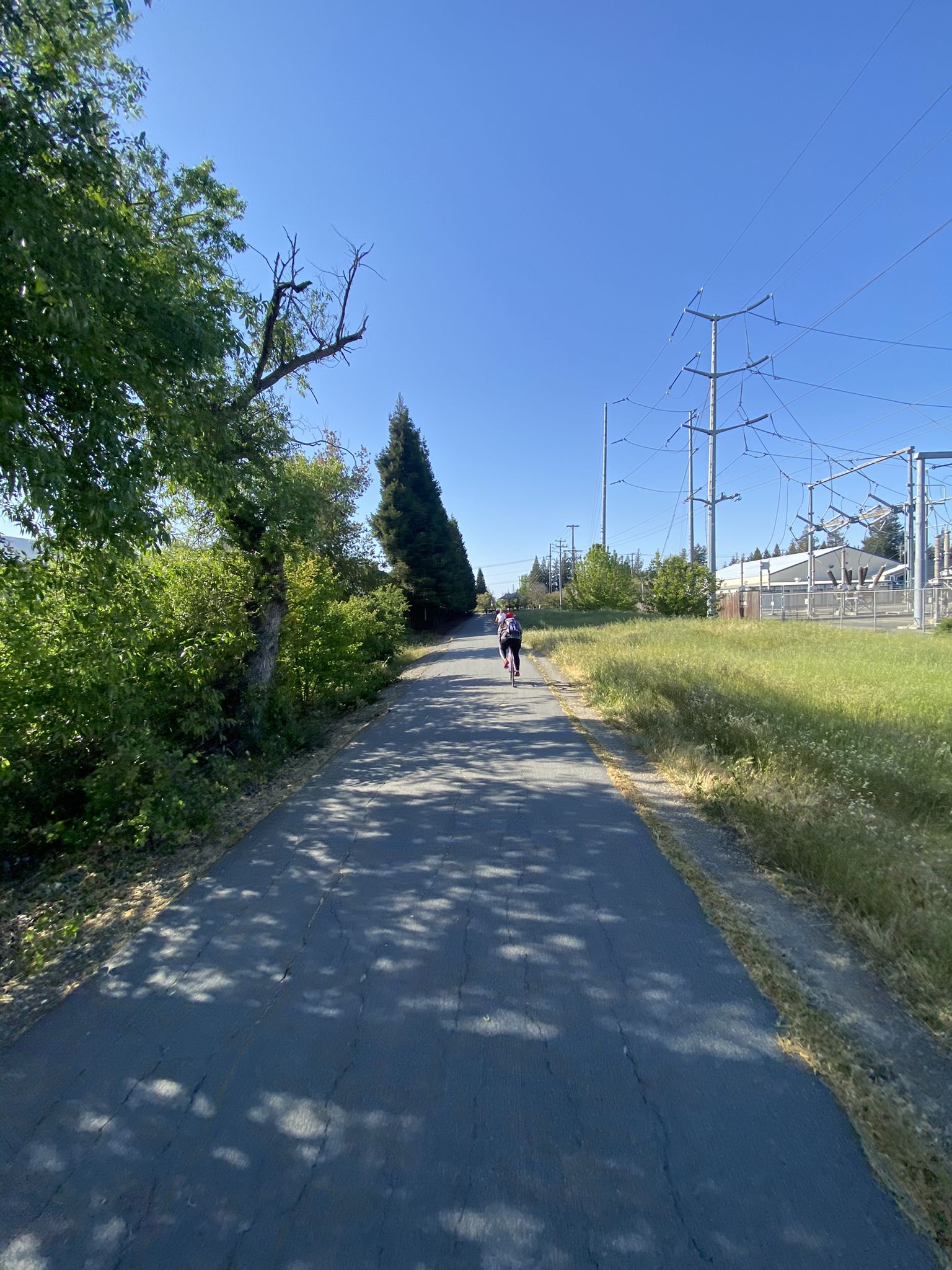 Paved path with a distant cyclist, next to power lines under a blue sky. - San Ramon iron horse trail loop from San Ramon