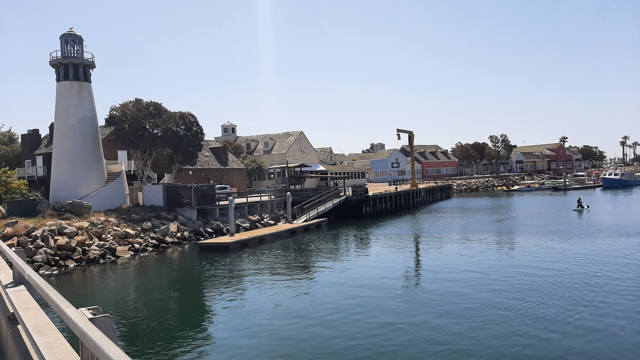 Lighthouse and waterfront buildings by calm water, with one person paddleboarding. - Balcom Canyon loop