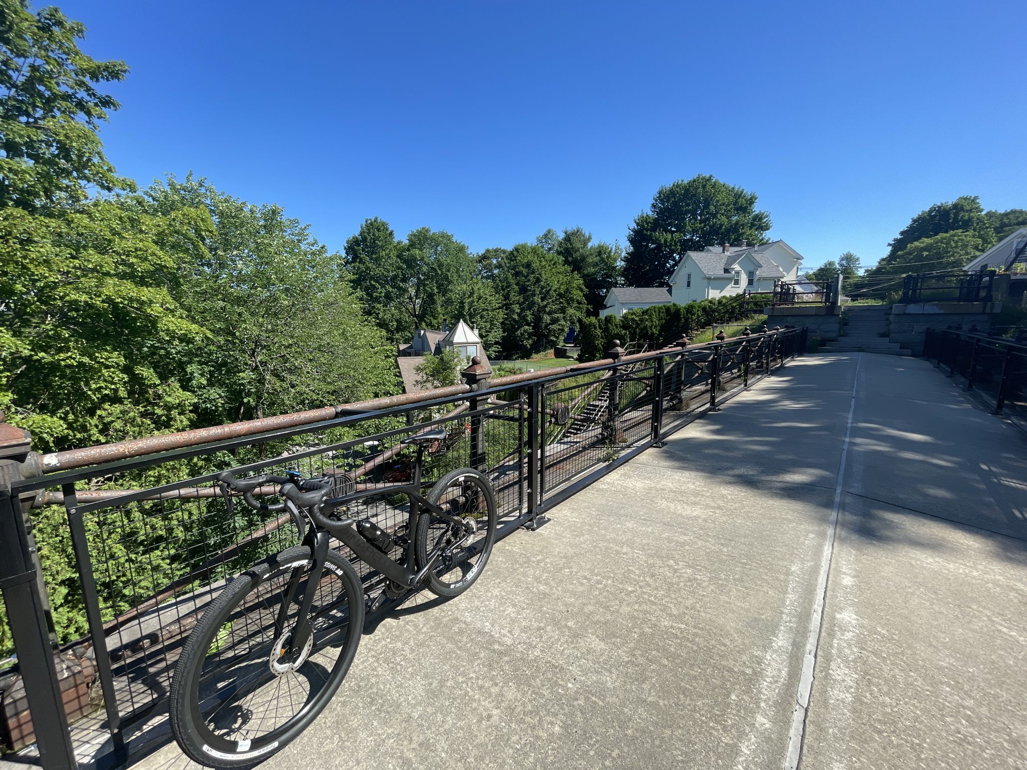 Black bicycle parked on a sunny bridge overlooking green trees and houses. - Cordingly Dam and Echo Bridge loop