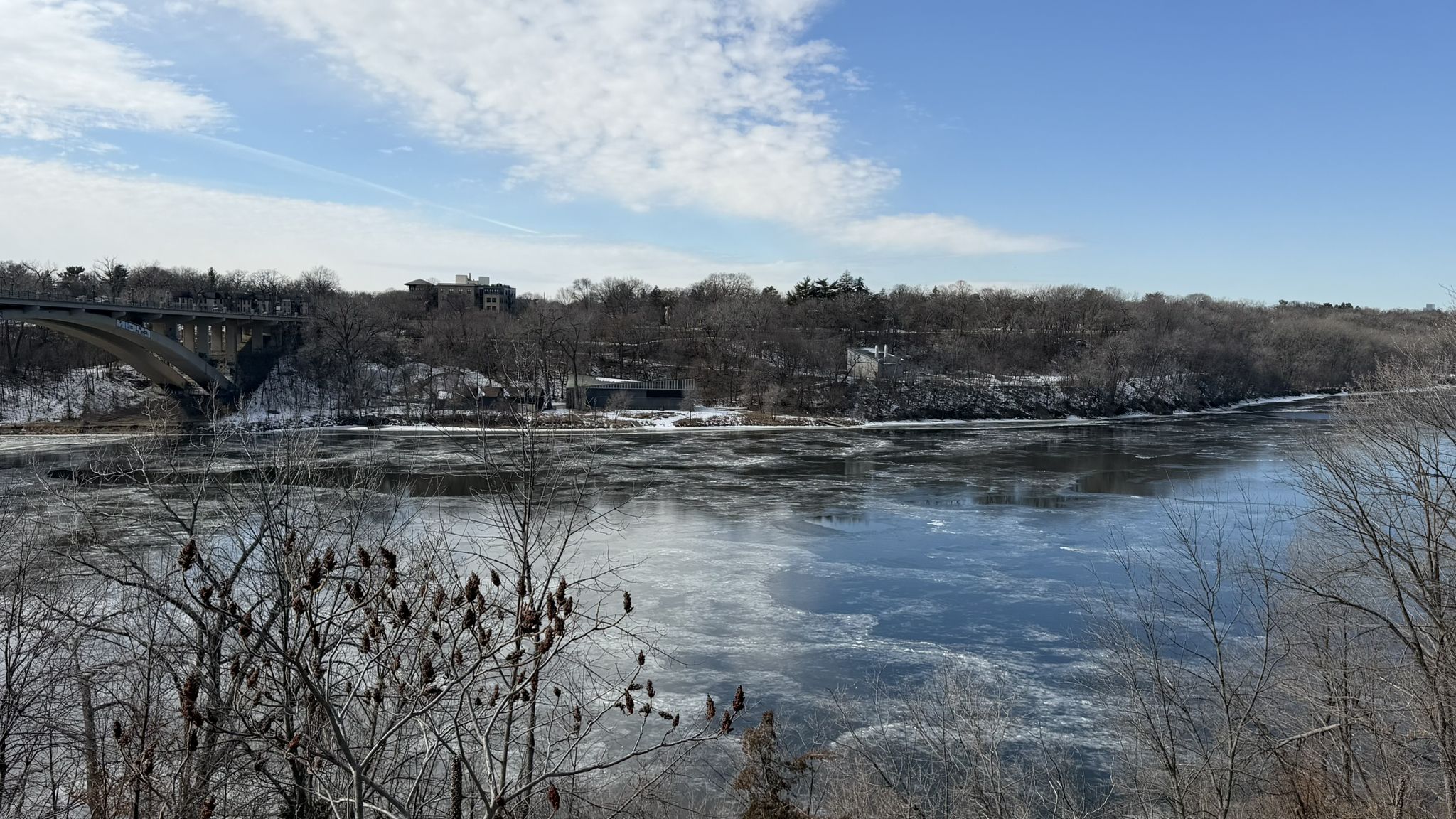 Icy river with snow-covered banks and bare trees under a bright blue sky. - Mississippi Gorge Trail loop