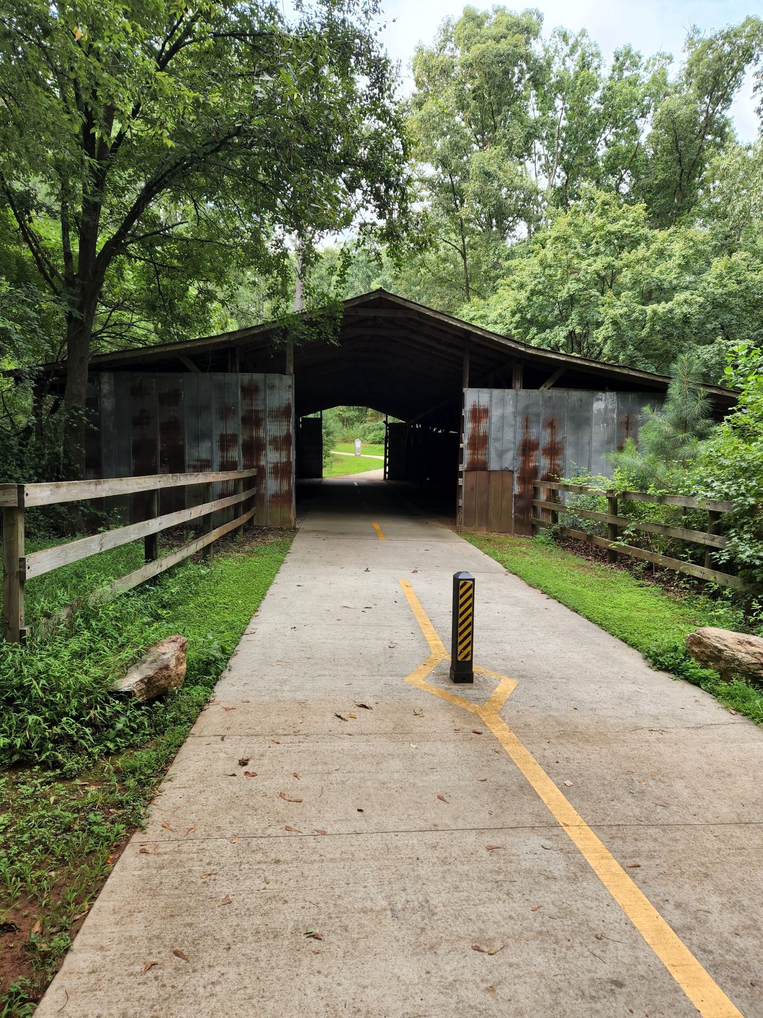 Concrete path with yellow lines leading into an open-sided barn structure. - Upper Alexander Lake Bridge loop from Panola Mountain State Park