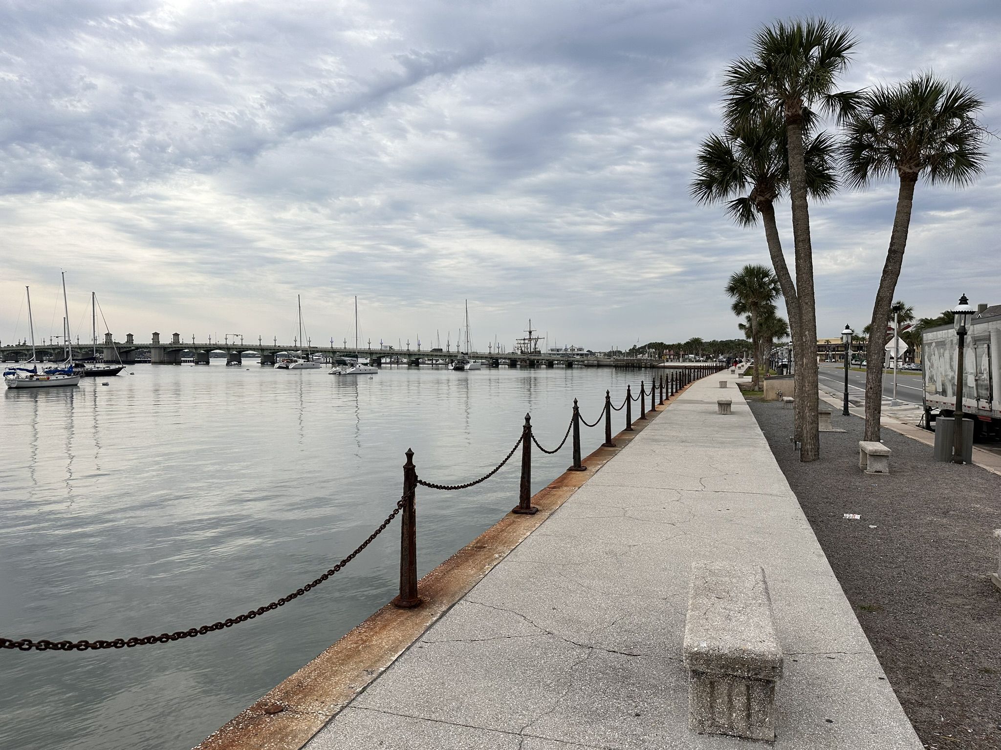 Waterfront promenade with boats and a distant bridge under cloudy sky. - Castillo de San Marcos – Cathedral loop from Saint Augustine