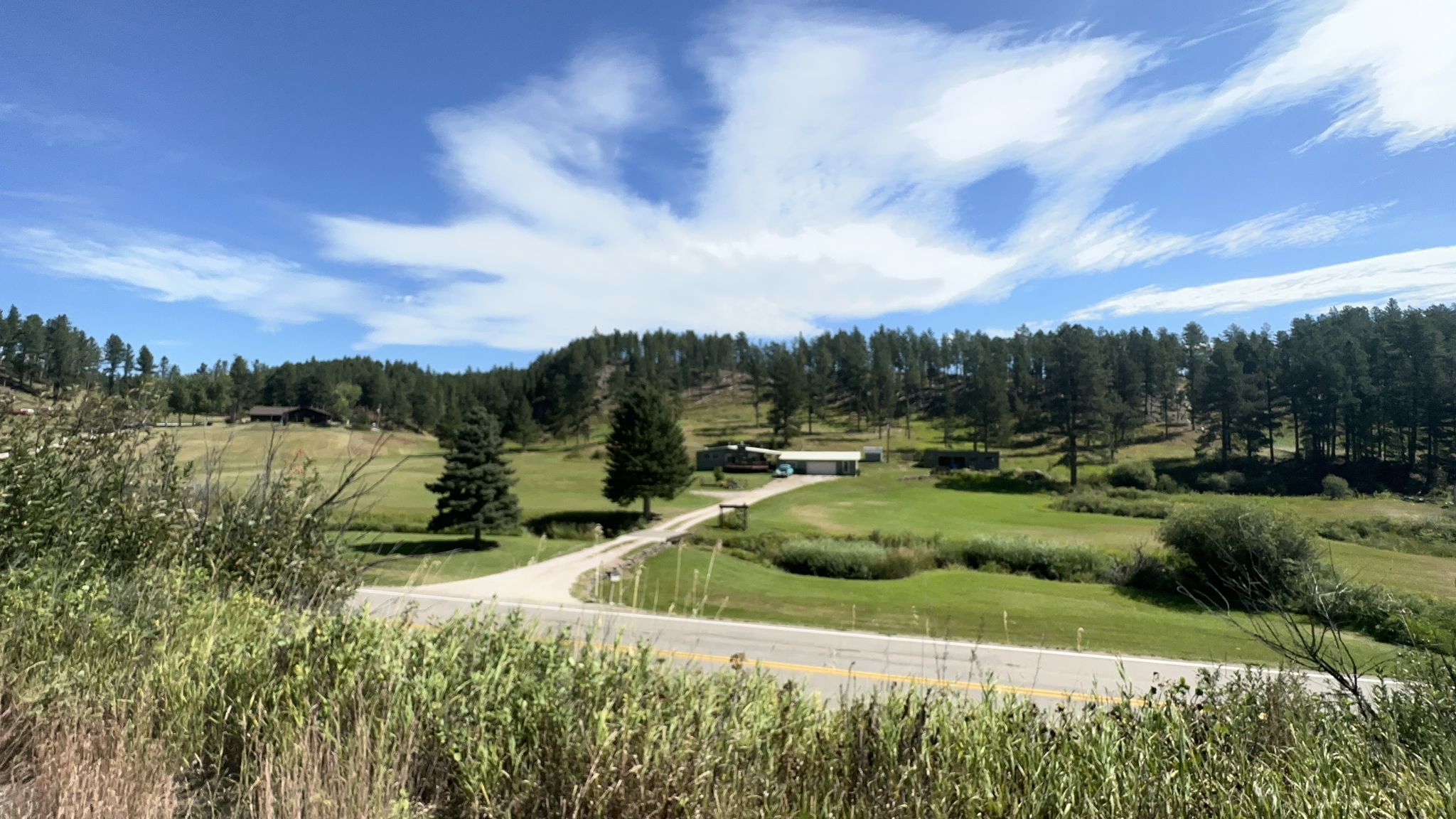 A winding road through a green valley with scattered houses and pine trees under a blue sky. - Hill City – Major Lake Park loop from Hill City