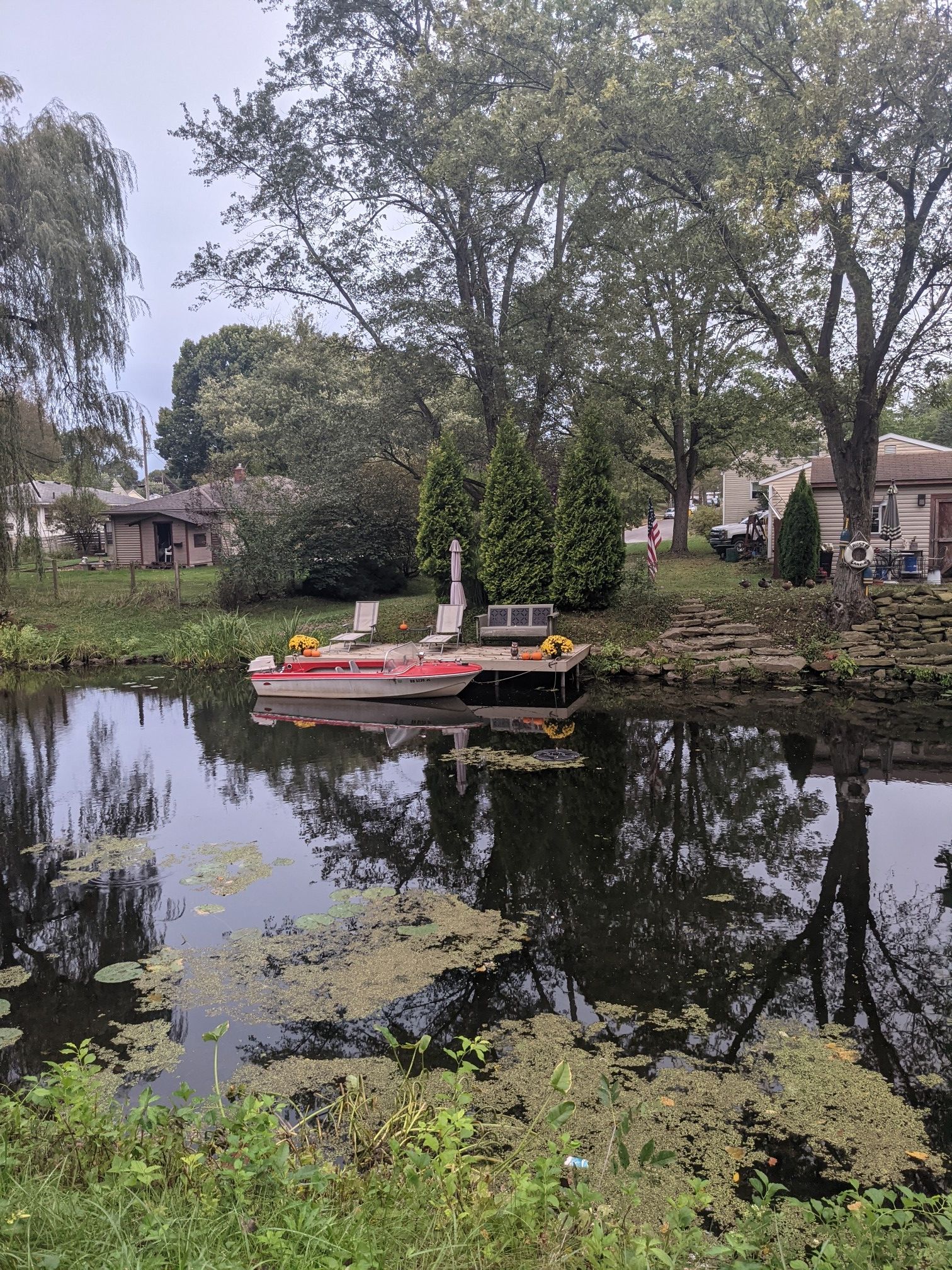 A small boat is docked on a calm, algae-covered waterway with houses and trees. - Canal Fulton Historic Disctrict – St Helena Heritage Park loop from Firestone Stadium