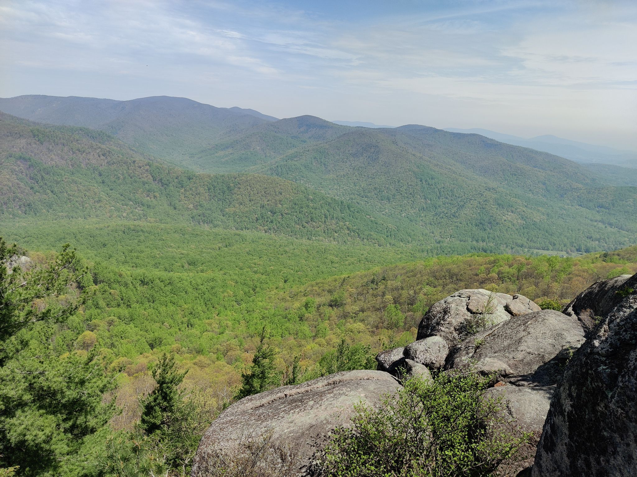 Expansive view of green forested mountains and large rock formations under bright sky. - Old Rag and Robertson Mountain Loop