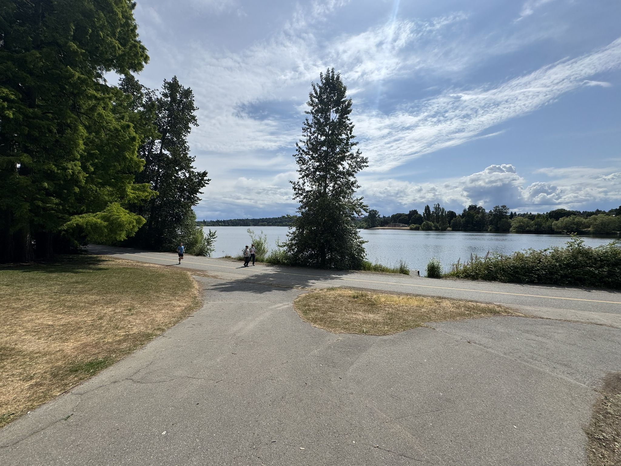 Paved path leading to a lake, with people walking under a partly cloudy sky. - Green Lake Outer Loop