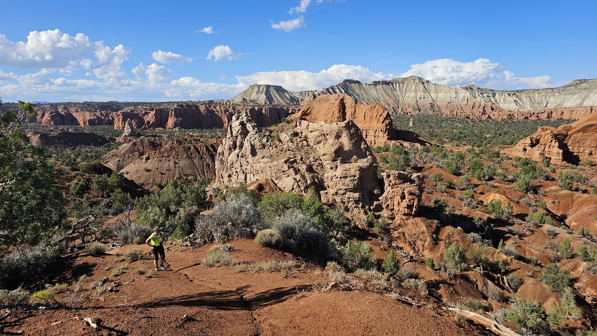 Hiker on a red rock overlook, vast desert landscape under a partly cloudy sky. - Panorama Trail Loop