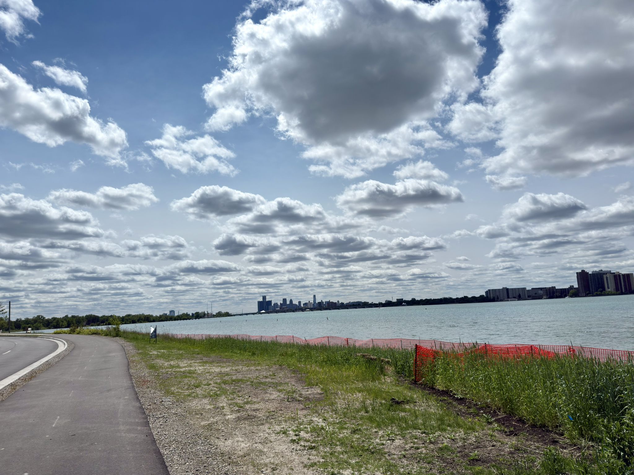 Paved path next to a wide river with a distant city skyline. - Belle Isle Beach – Belle Isle Park loop from Roberts Riverwalk Hotel
