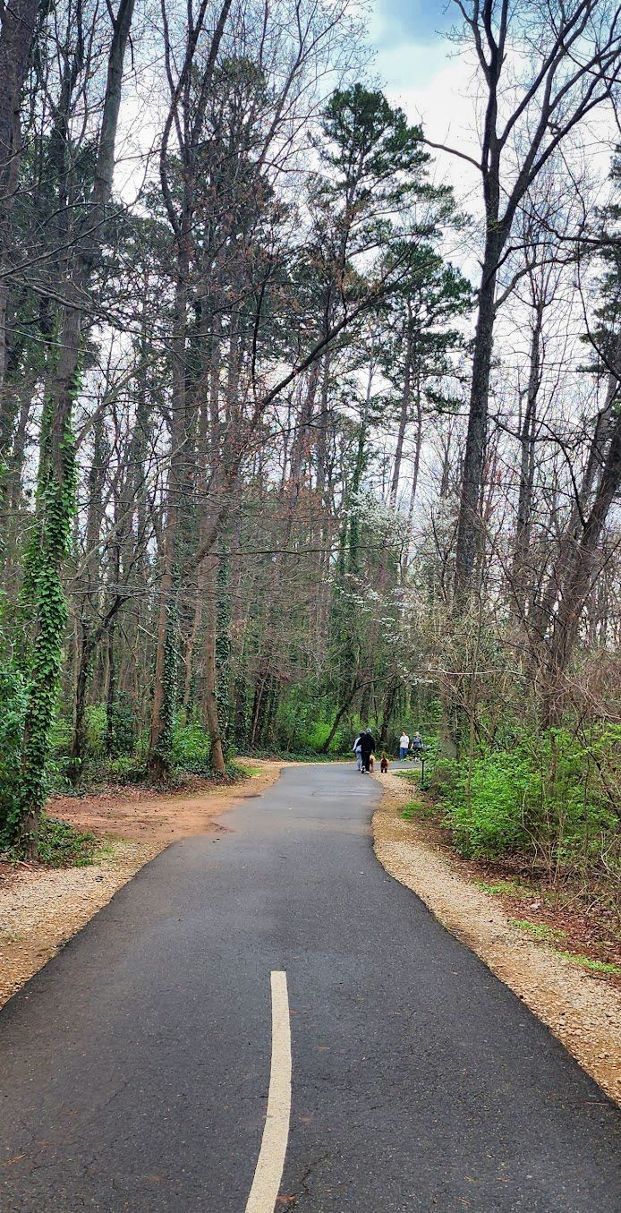 Paved path with white line leads into a forest with distant walkers. - Great Circle of Charlotte loop
