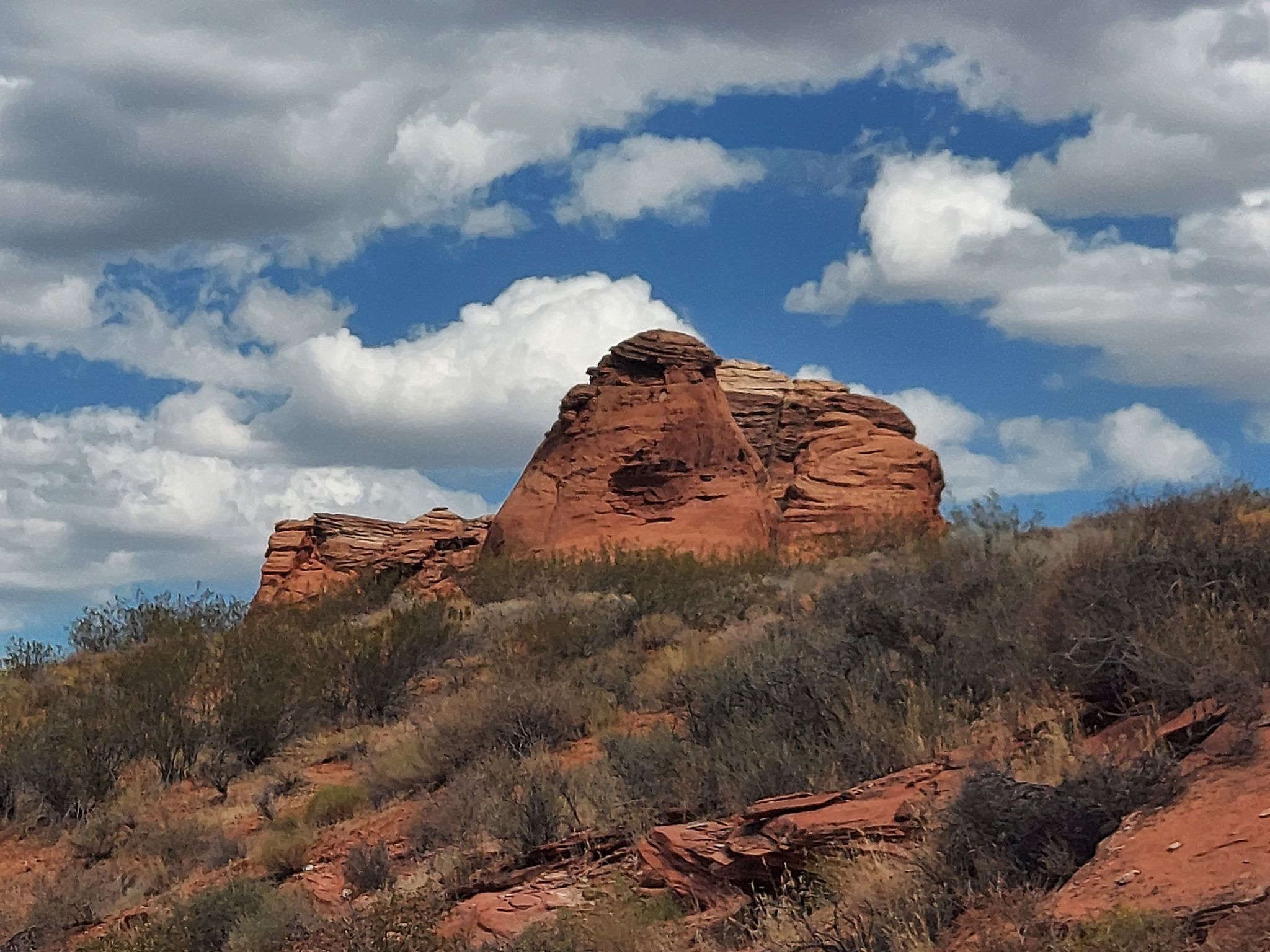 Large red rock formation on a hill under a partly cloudy sky. - Prospector and Church Rocks Loop