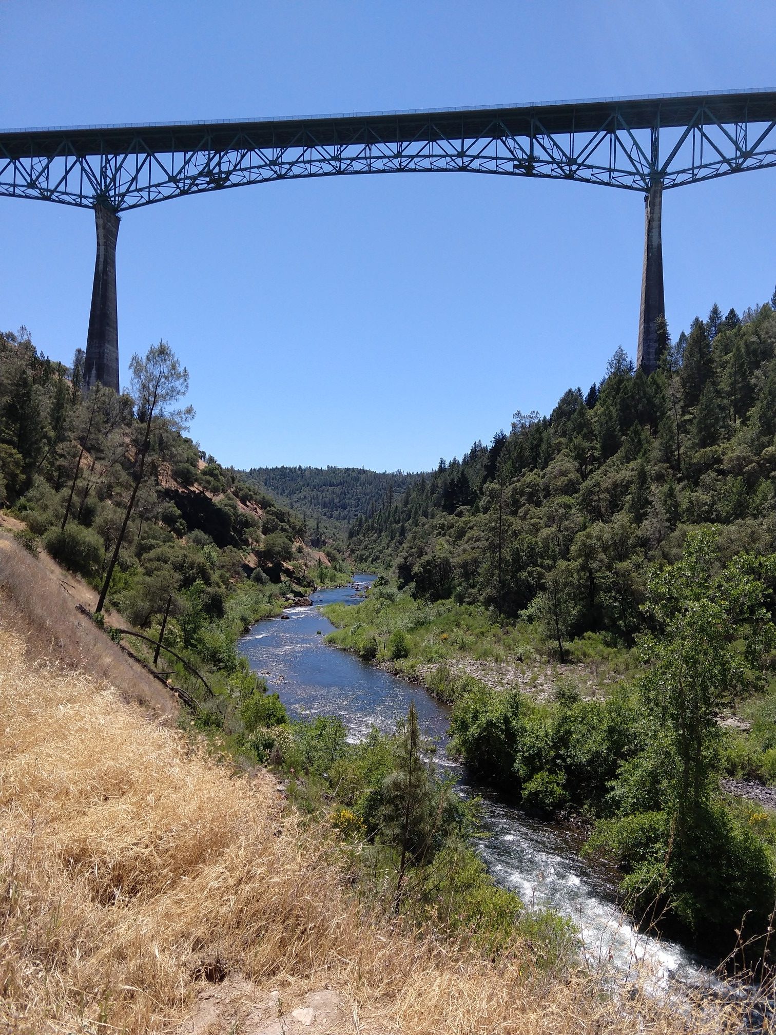 A large bridge spans a river flowing through a dry, forested canyon. - Clementine Trail