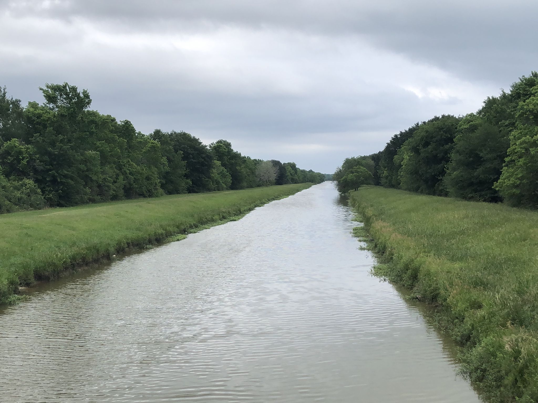 A wide canal flows between green grassy banks under an overcast sky. - George Bush Park Hike & Bike Trail Loop from Sugar Land