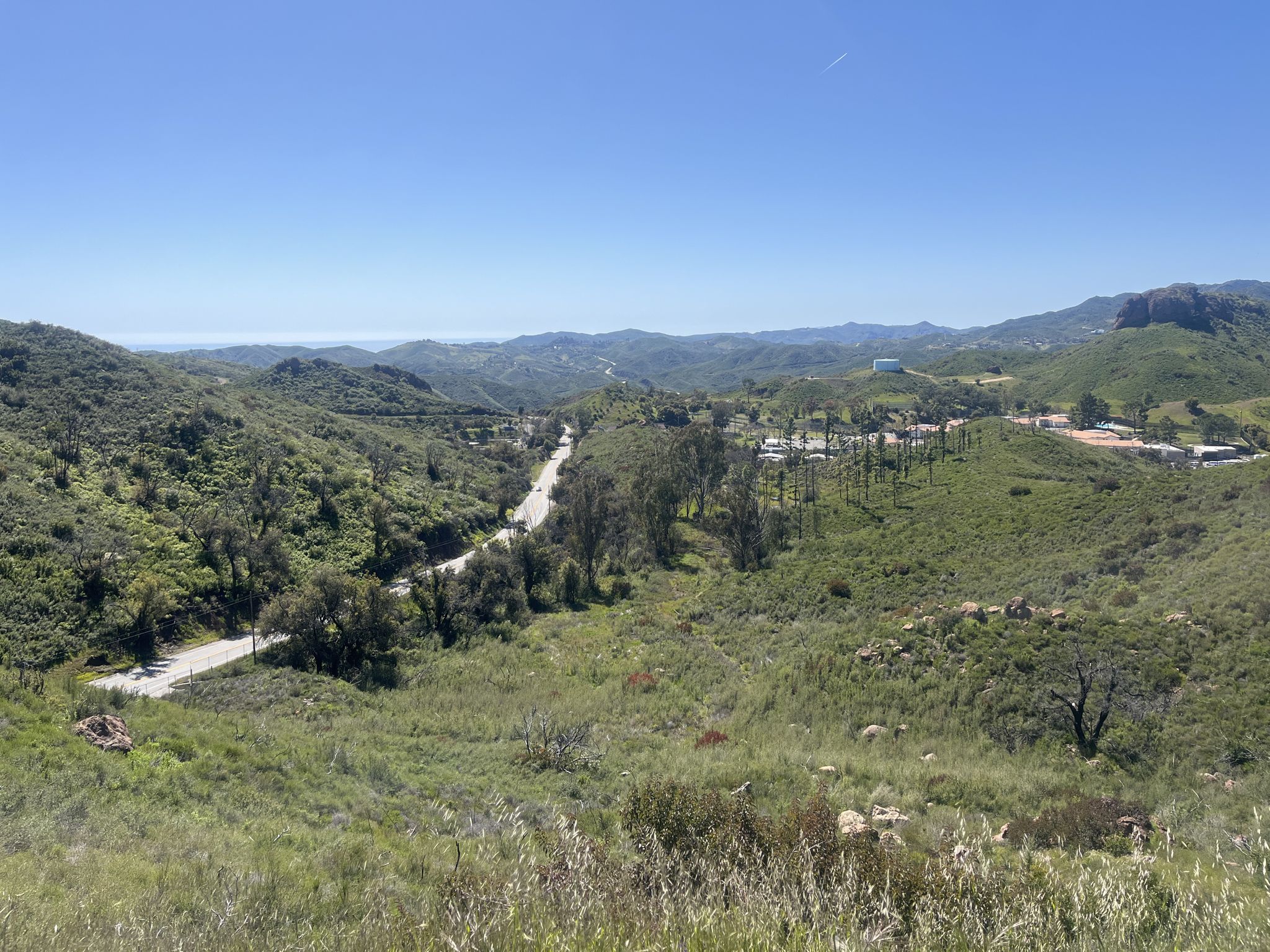 A winding road cuts through lush green hills on a clear sunny day. - Encinal Canyon Loop
