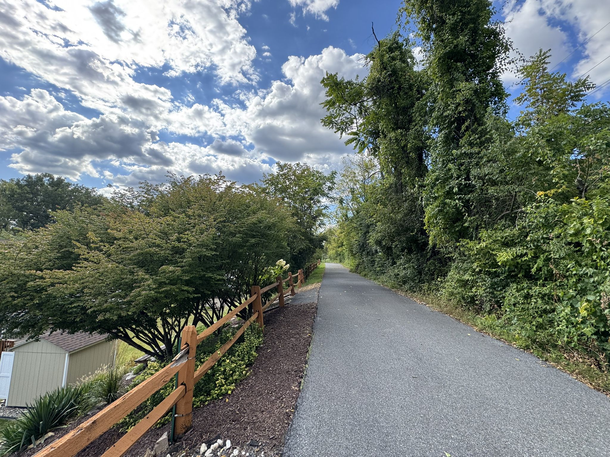 A paved path runs alongside a wooden fence under a bright, cloudy sky. - Ironton Rail Trail – Coplay Creek loop from Northampton