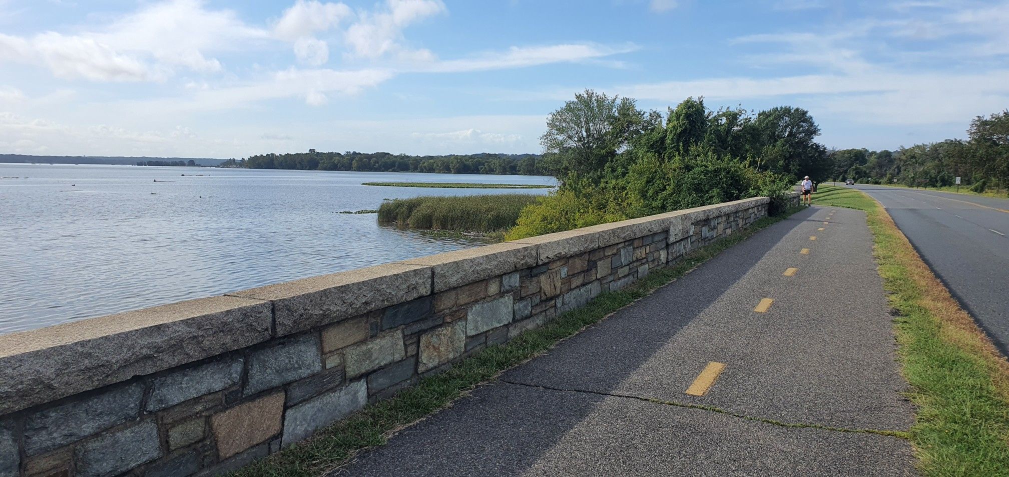 Paved path beside a stone wall overlooking a wide body of water. - Wooden bridge – Mount Vernon Trail loop from Alexandria