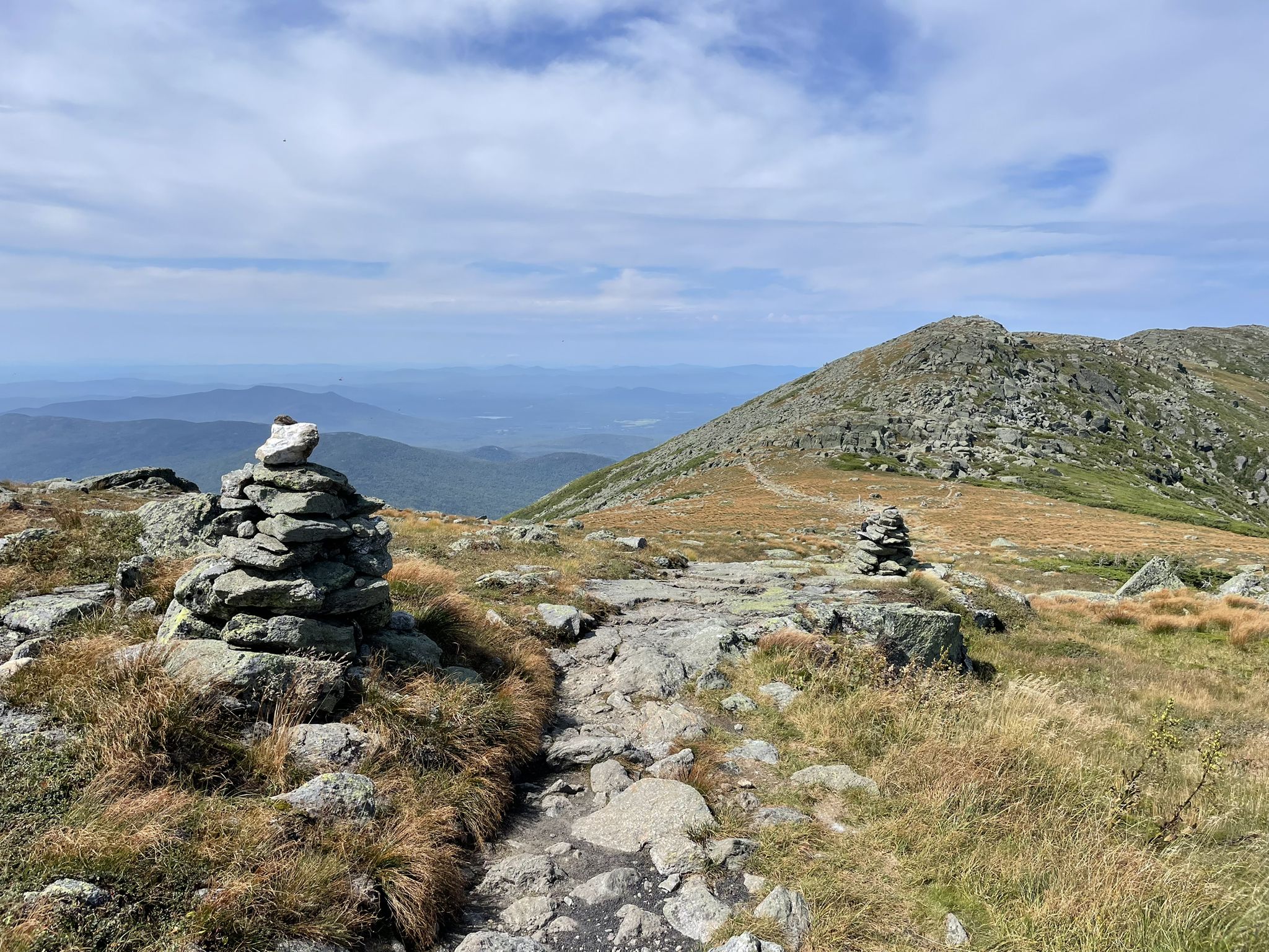 Rocky mountain path with stone cairns and grassy slopes under a cloudy sky. - Gulfside Trail