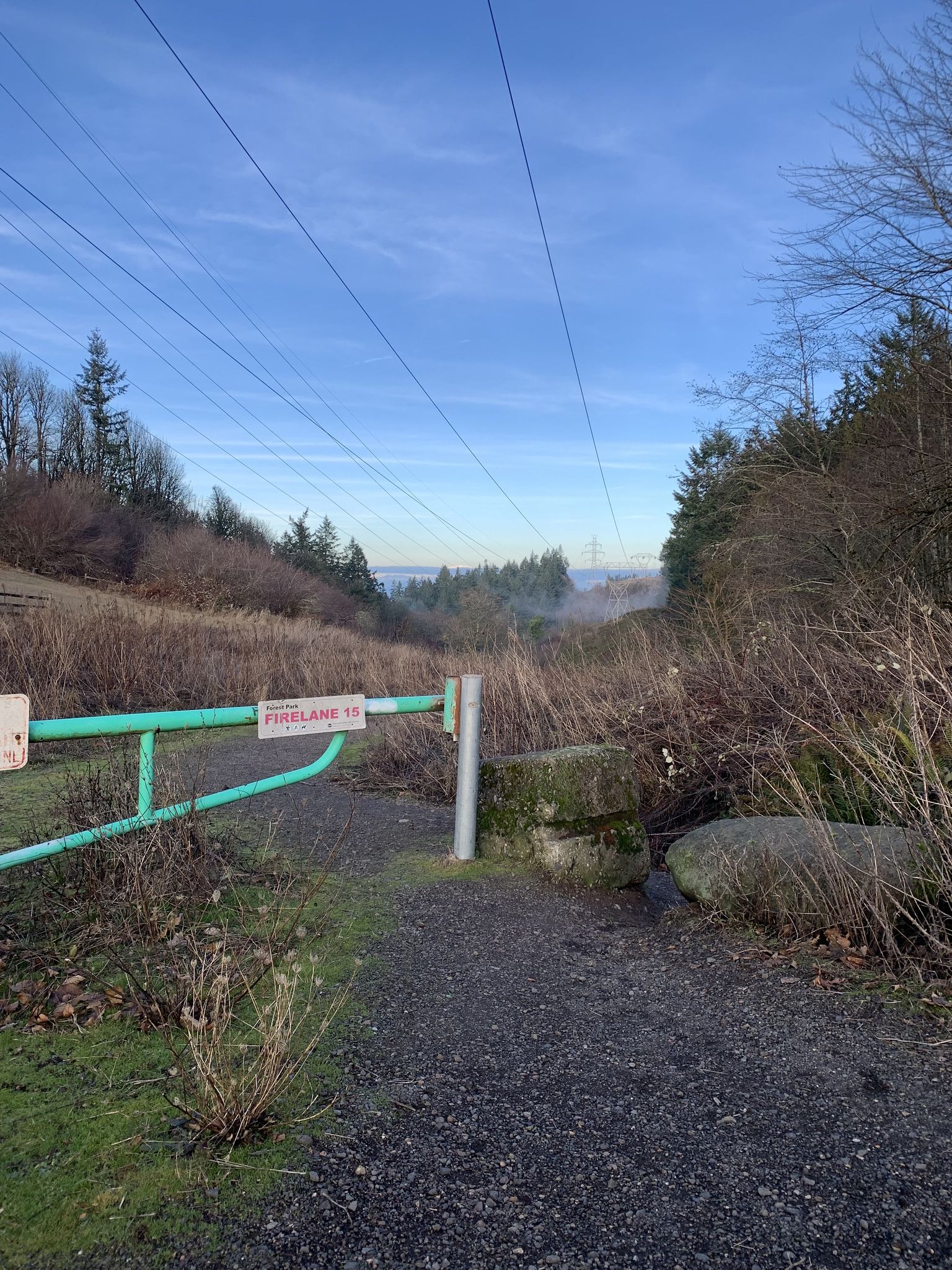 A green gate blocks a dirt road under power lines, with a hazy view. - Bethany Lake – Rock Creek Trail loop from Willow Creek/Southwest 185th Avenue Transit Center