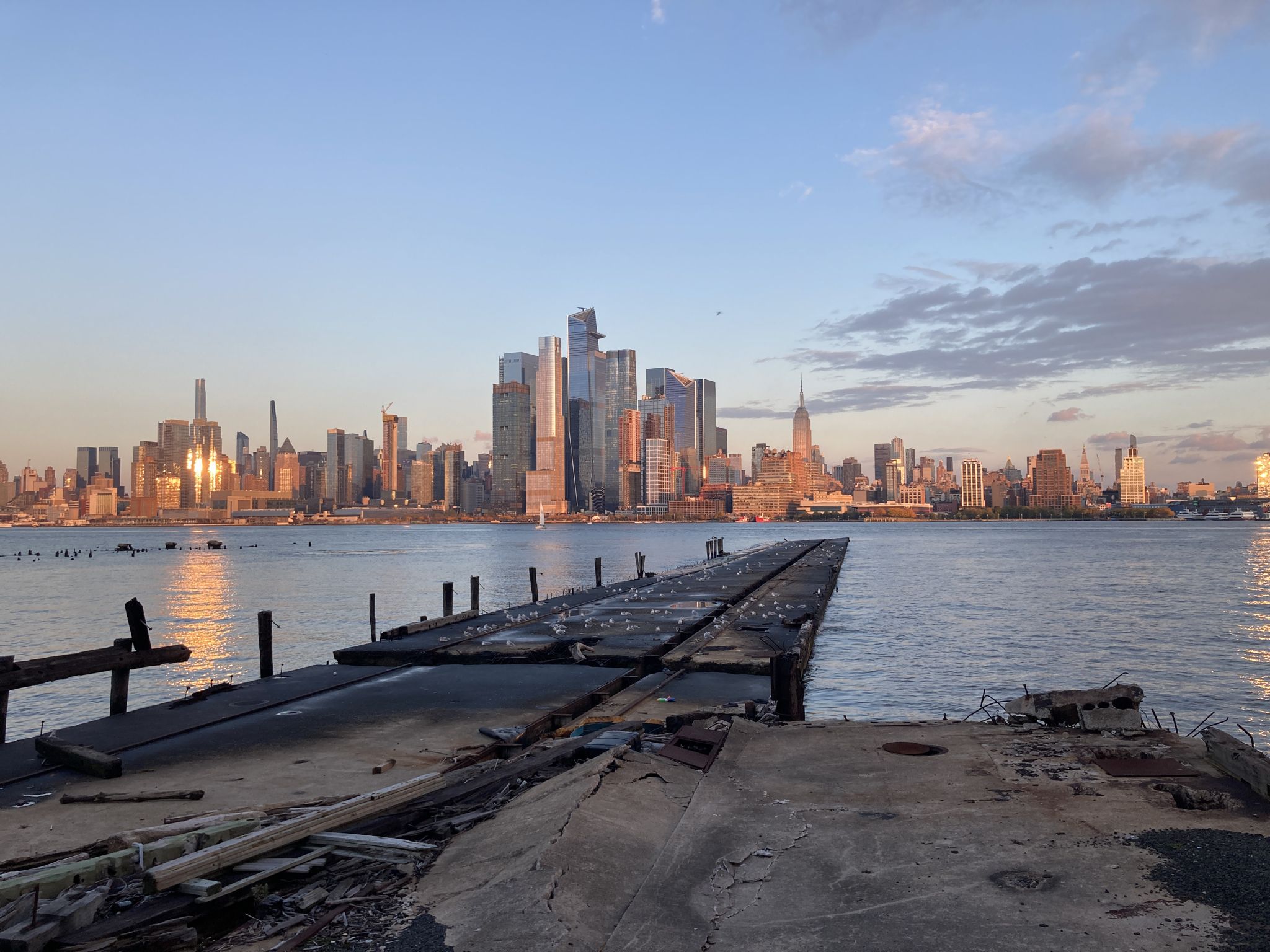 Dilapidated pier extends into water, city skyline glows golden at sunset. - Weehawken Cove loop from Lincoln Harbor