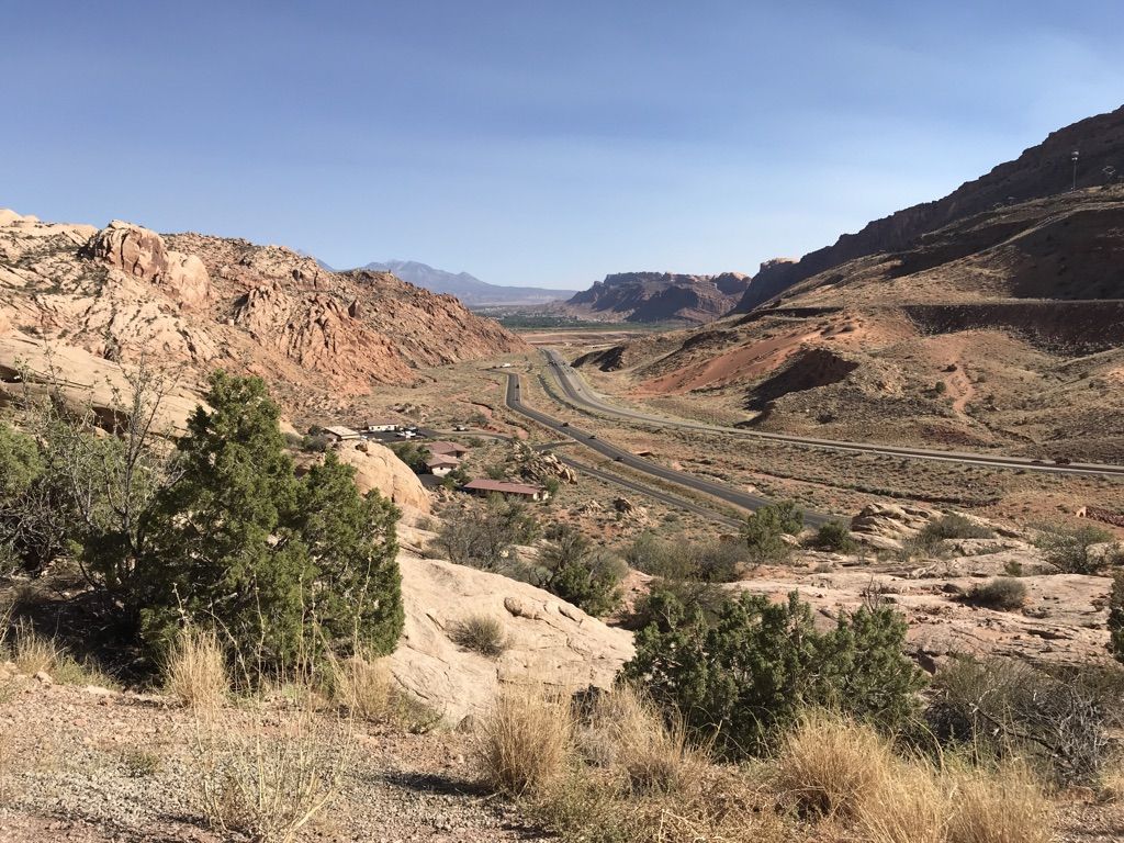 A highway winds through a wide desert valley with distant mountains. - Petrified Dunes Viewpoint – Courthouse Towers Viewpoint loop from Salt Wash Trailhead Parking