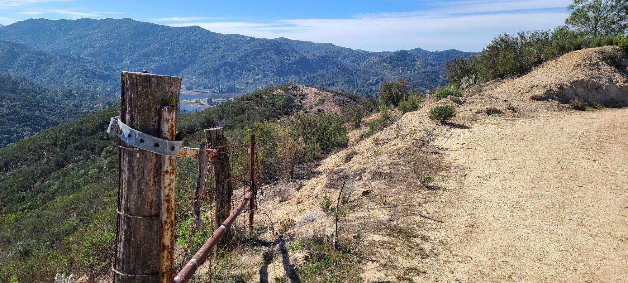 A dirt path next to old fence posts overlooking distant mountains. - Blinn Trail