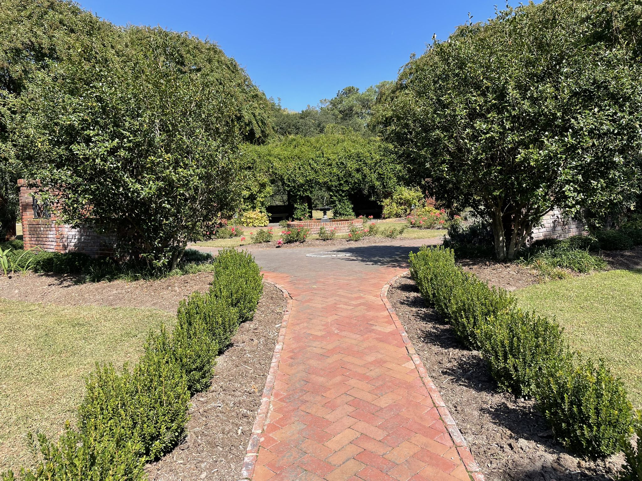 A brick path forks in a sunny, green garden with lush trees. - Elizabeth River Trail and Ocean View Loop