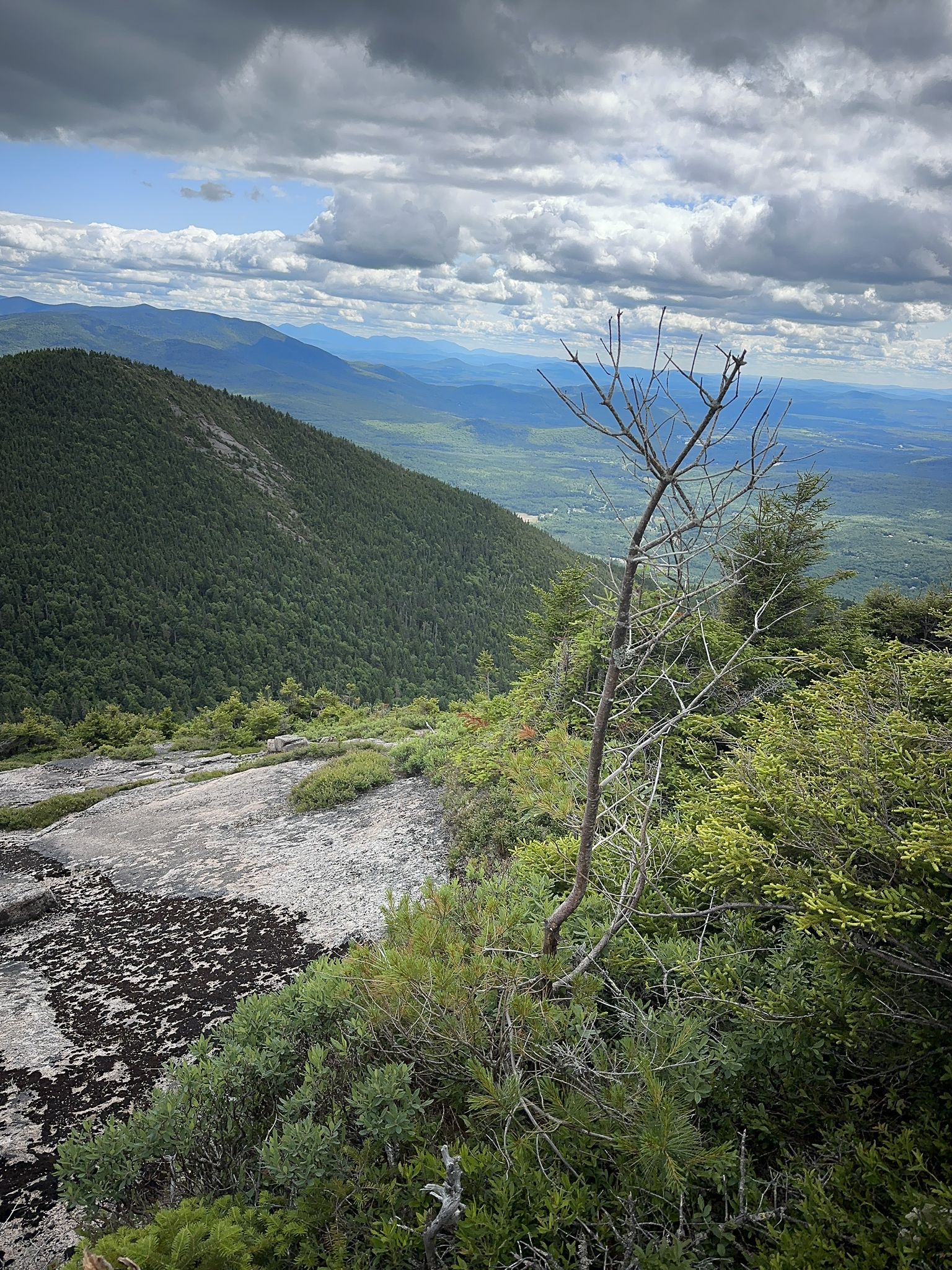 Steep mountain slope with rocky outcrop, distant valleys under cloudy sky. - Percy Peaks Trail