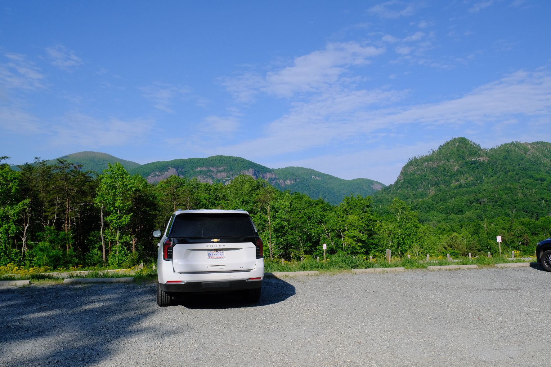 White SUV parked in a lot with green mountains under a bright blue sky. - Rumbling Bald Loop Trail