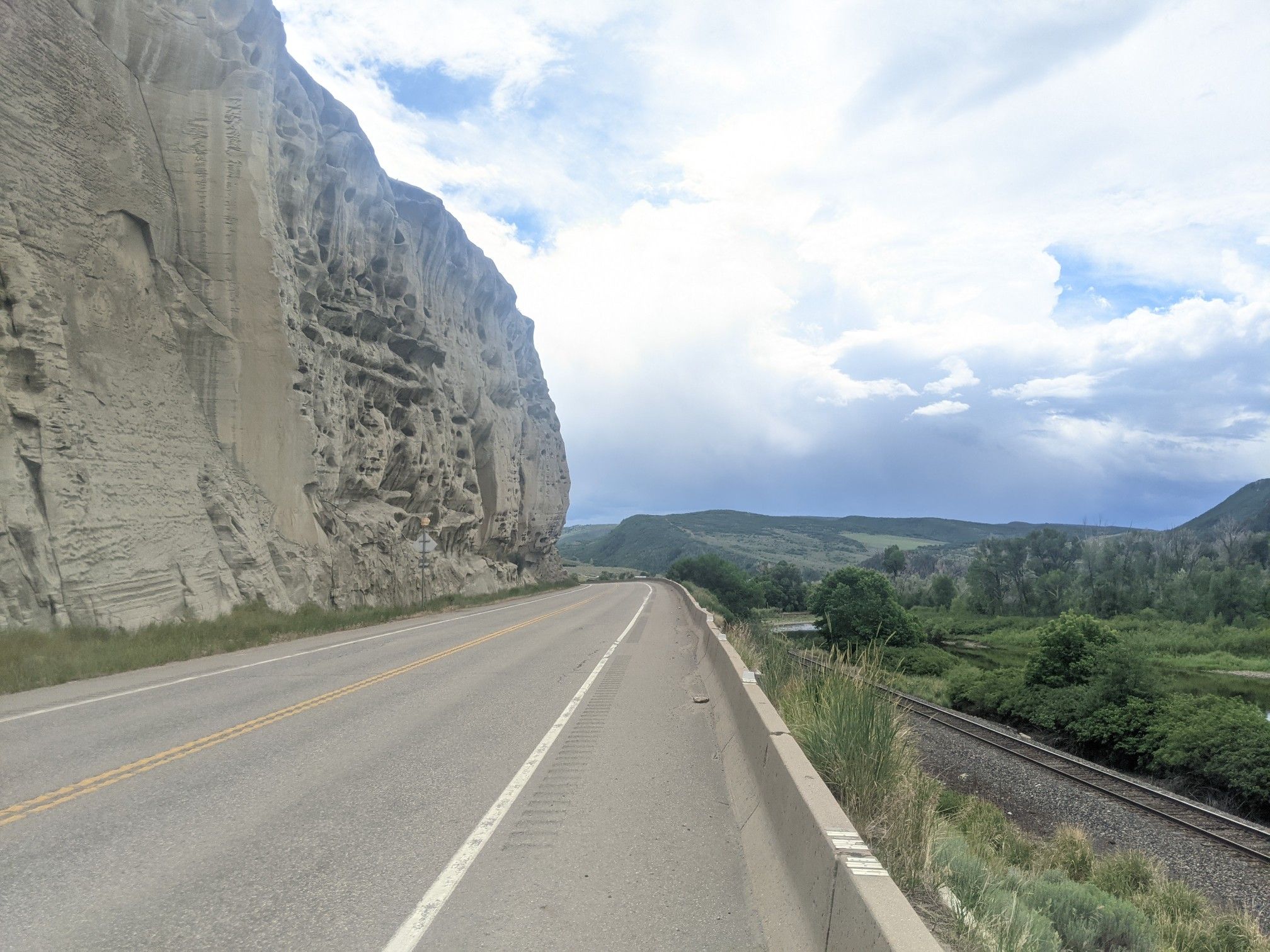 A highway runs alongside a towering rock cliff and a railway track. - Hayden Loop