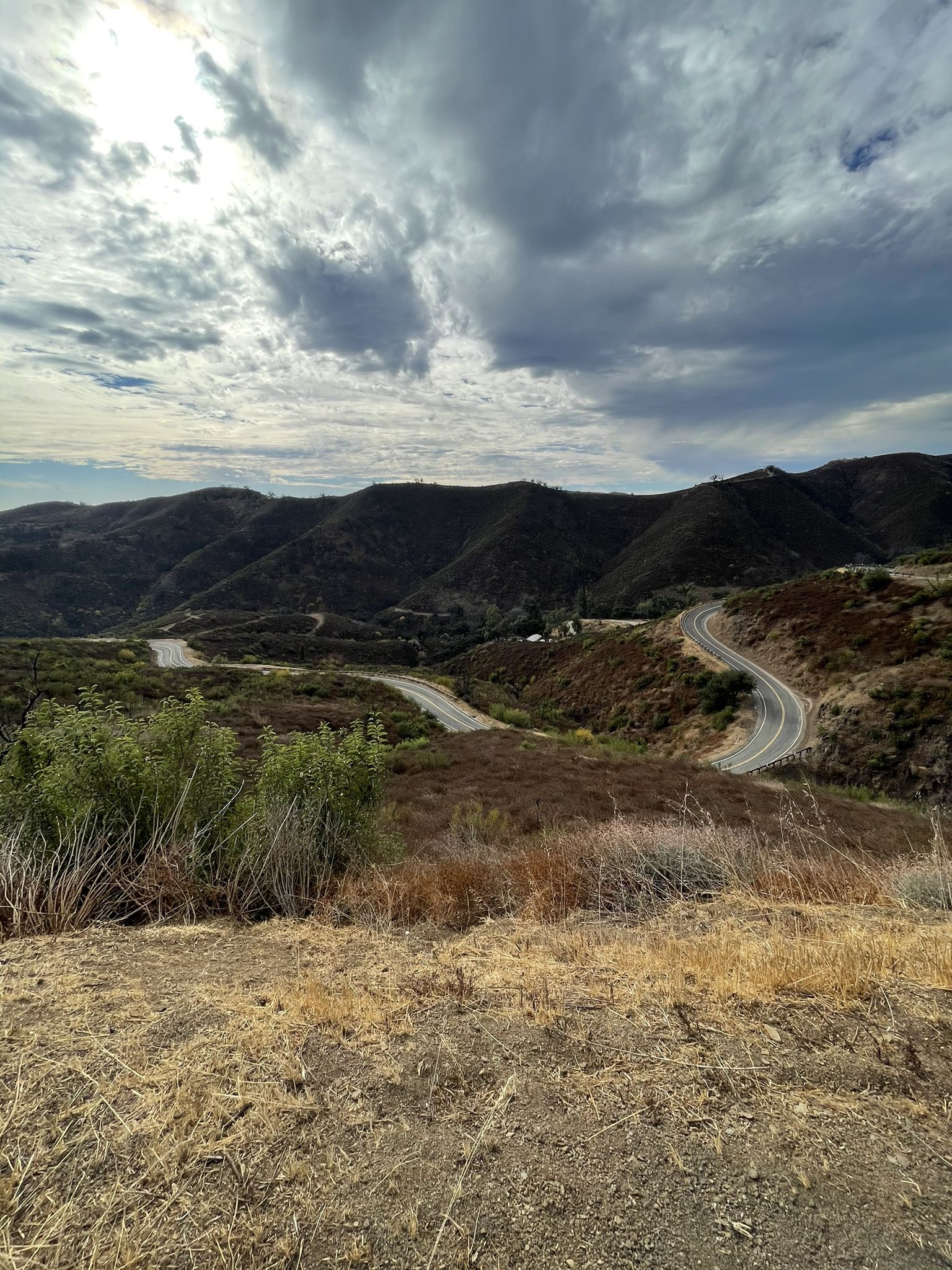 Winding road through arid mountains under a dramatic cloudy sky. - Dan Blocker County Beach – Dan Blocker Beach loop from Dan Blocker County Beach
