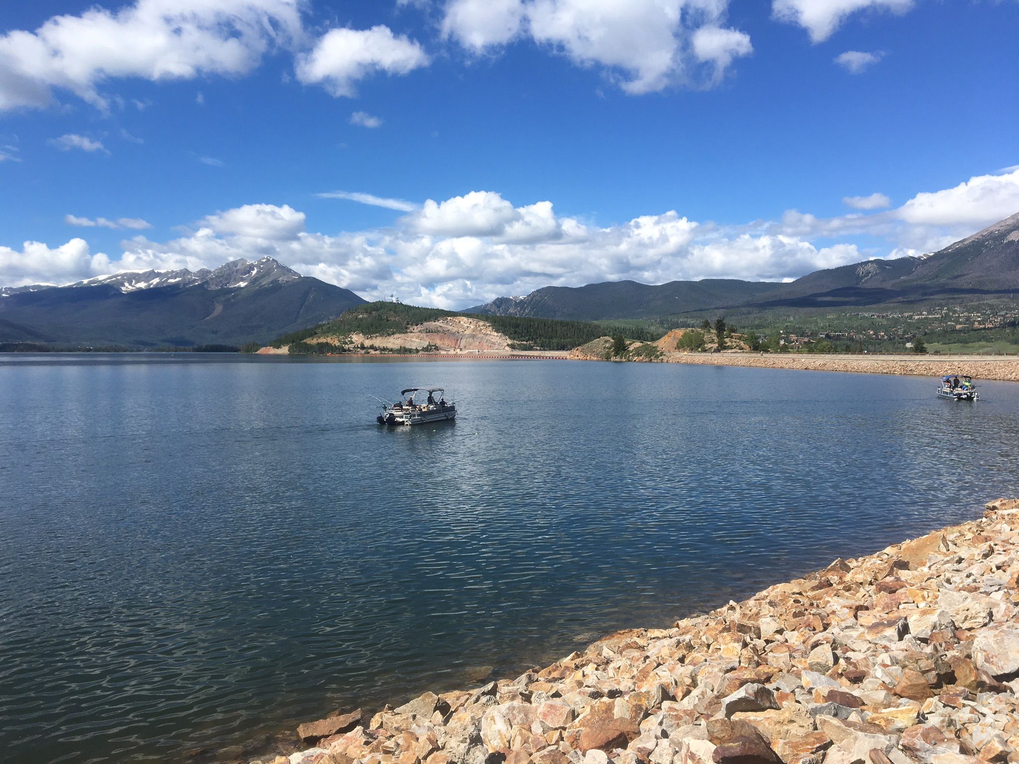 Two boats on a sunny lake with rocky shore and distant mountains. - Dillion Dam via Ryan Gulch