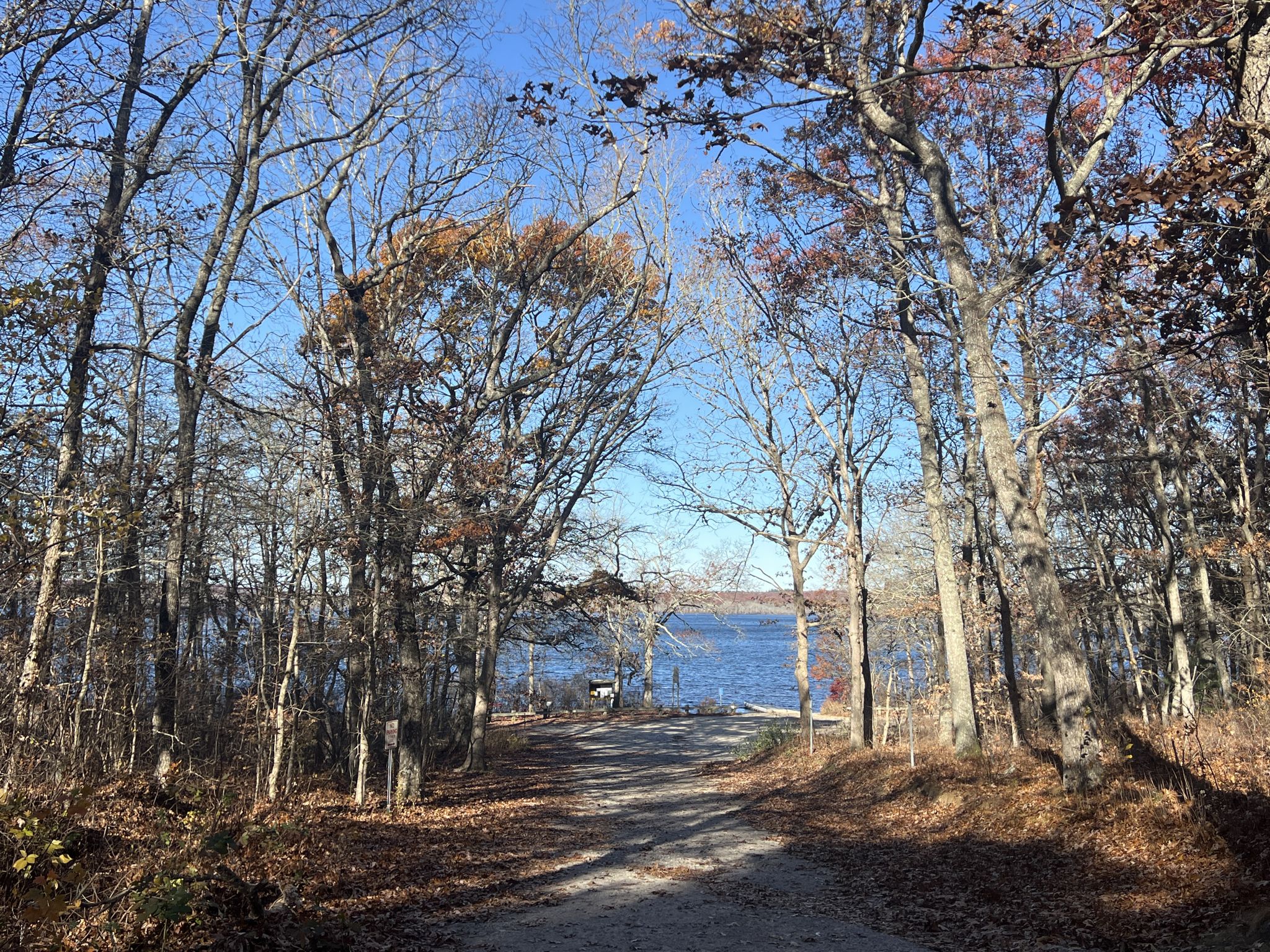 A dirt road descends through bare trees towards a large body of water. - Richmond to Hope Valley Loop