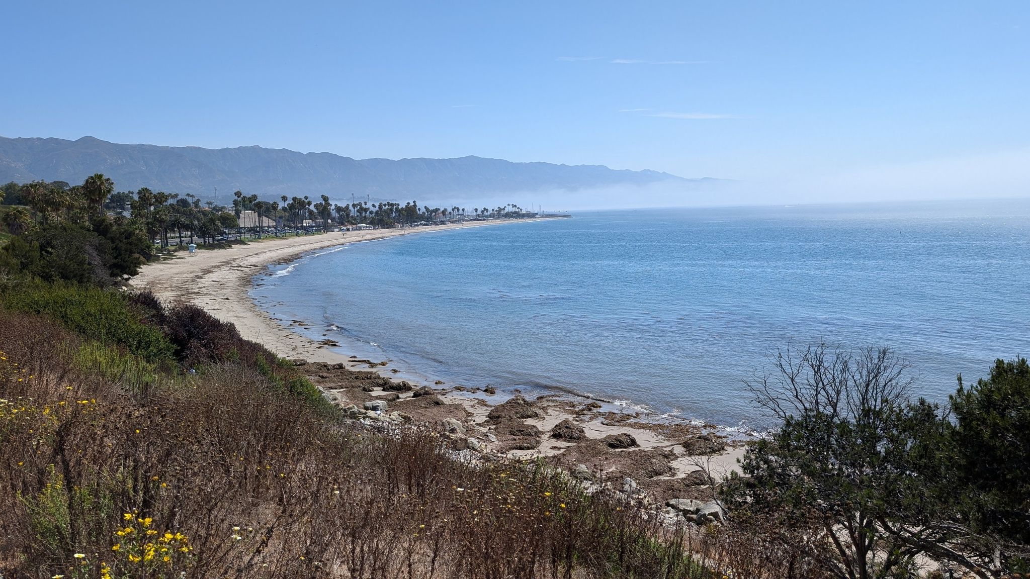 Panoramic view of a long sandy beach curving along the ocean under clear skies. - Hope Ranch Loop