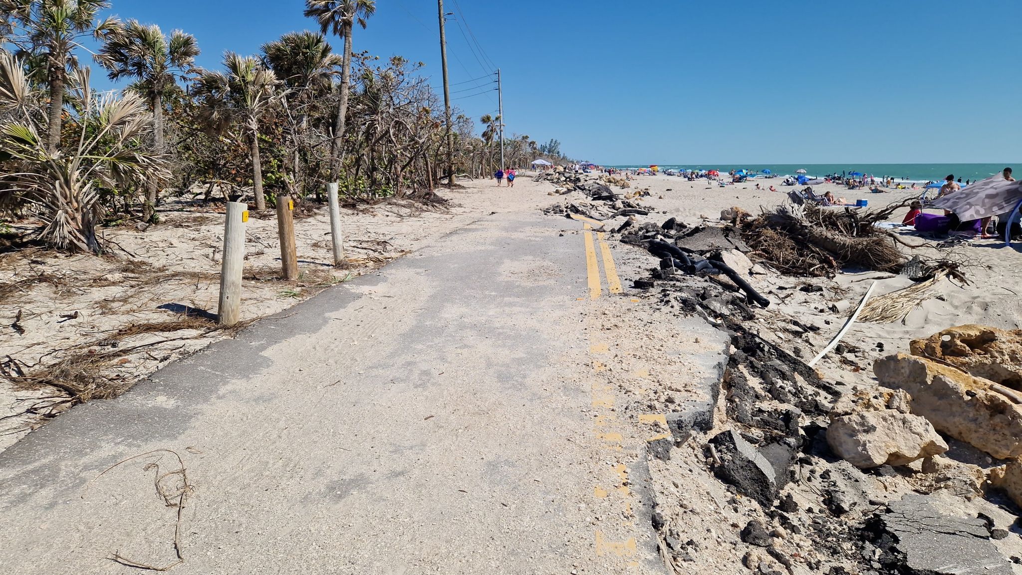 Damaged paved path next to a sunny beach with distant people. - Manasota Key