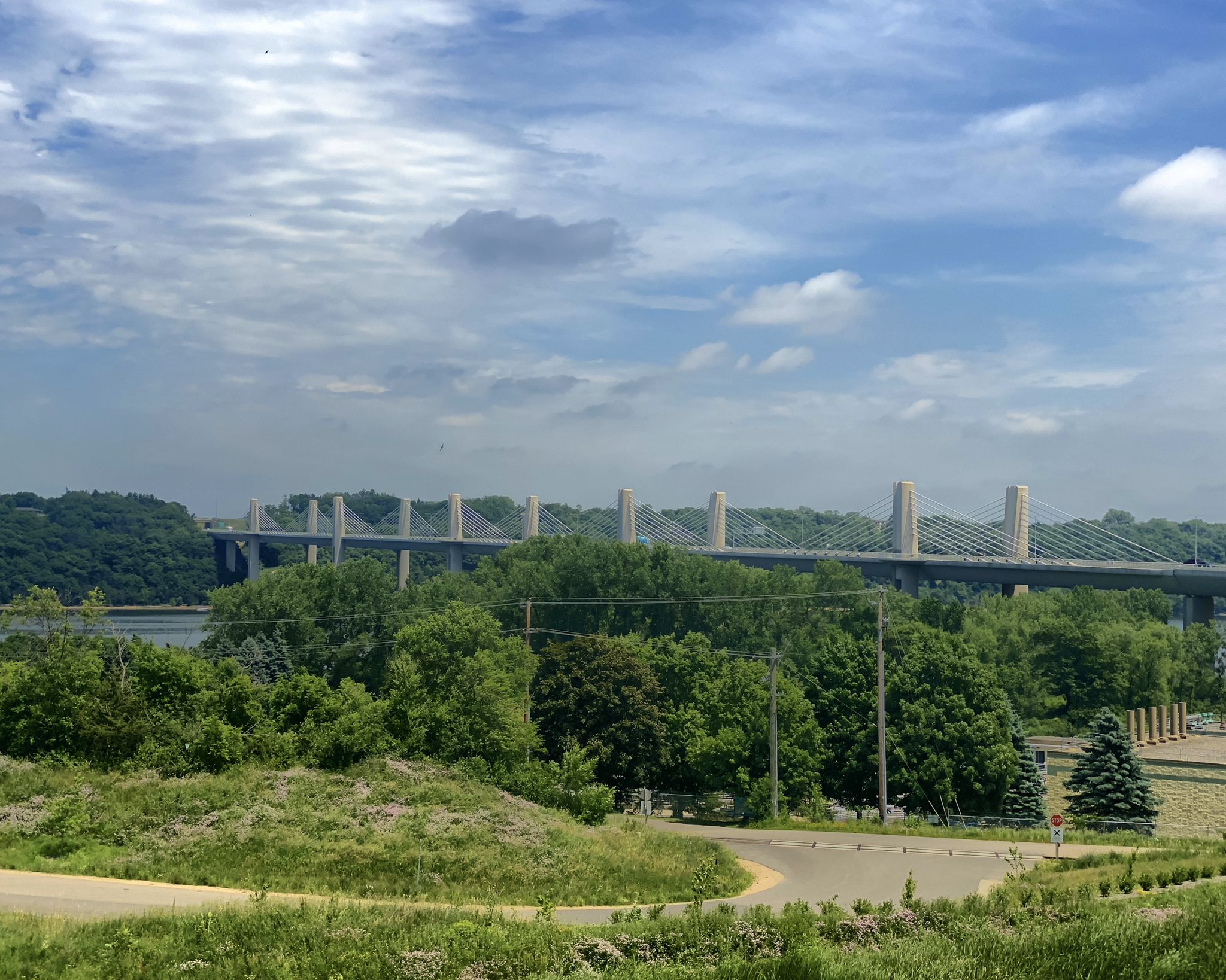 Distant bridge visible over green trees and hills, cloudy sky. - Saint Croix Crossing Loop Trail